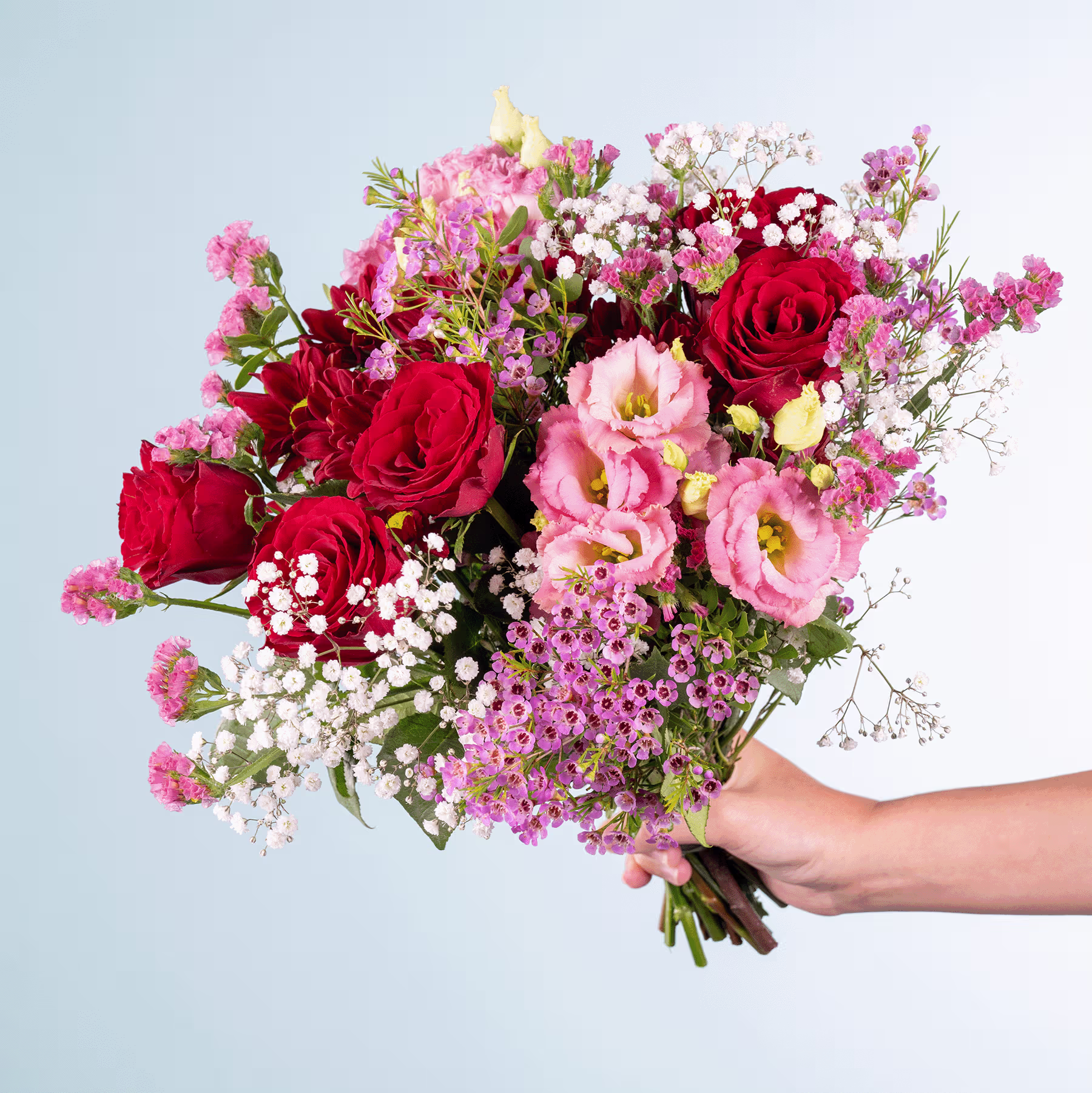 Ein leuchtender Strauß roter Rosen, rosa Nelken und zarter Schleierkrautblüten, den eine Person vor einem schlichten blauen Hintergrund in der Hand hält. (Beschreibungstext KI-generiert)
