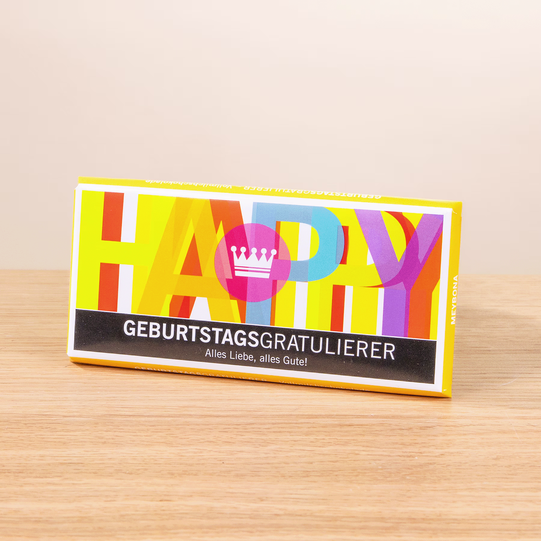 Auf einer Holzoberfläche steht eine bunte „Happy Birthday“-Grußkarte mit einem Kronensymbol. (Beschreibungstext KI-generiert)