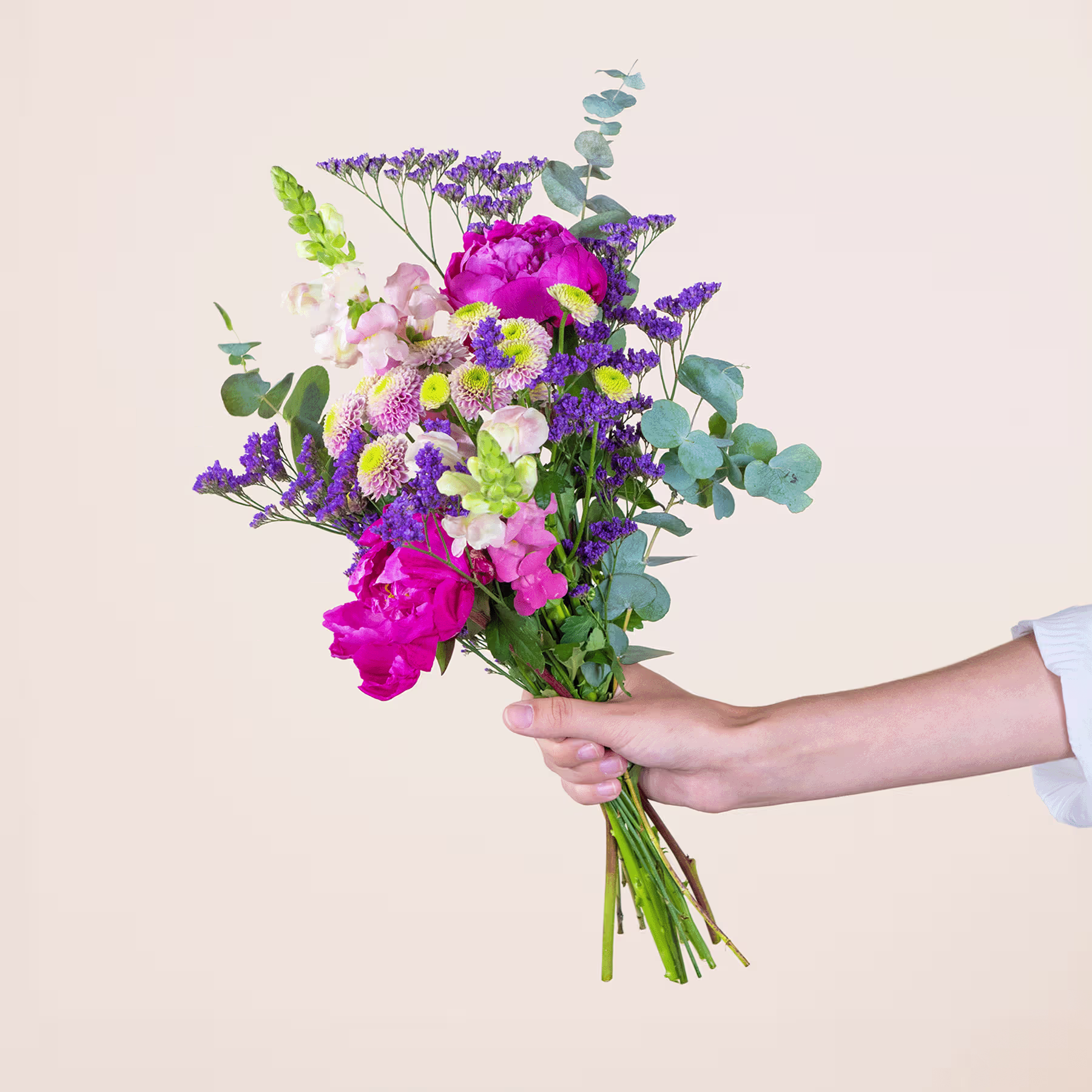 Ein leuchtender Strauß bunter Blumen, darunter rosa Pfingstrosen, lila Lavendel und grünes Laub, wird vor einem schlichten, hellen Hintergrund in den Händen einer Person gehalten. (Beschreibungstext KI-generiert)