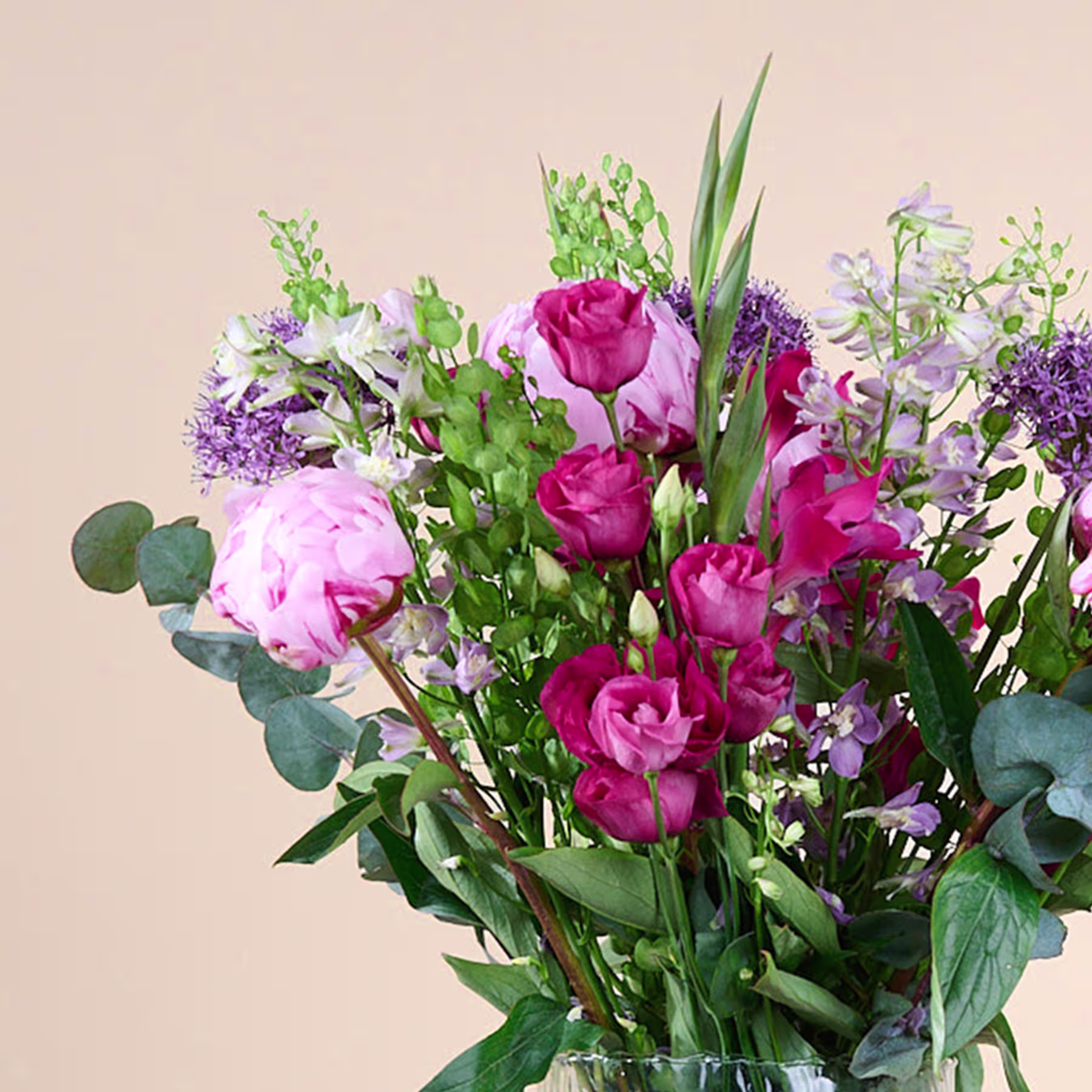 Ein lebendiger Strauß aus rosa Rosen, lila Blumen und üppigem Grün vor einem neutralen beigen Hintergrund. (Beschreibungstext KI-generiert)