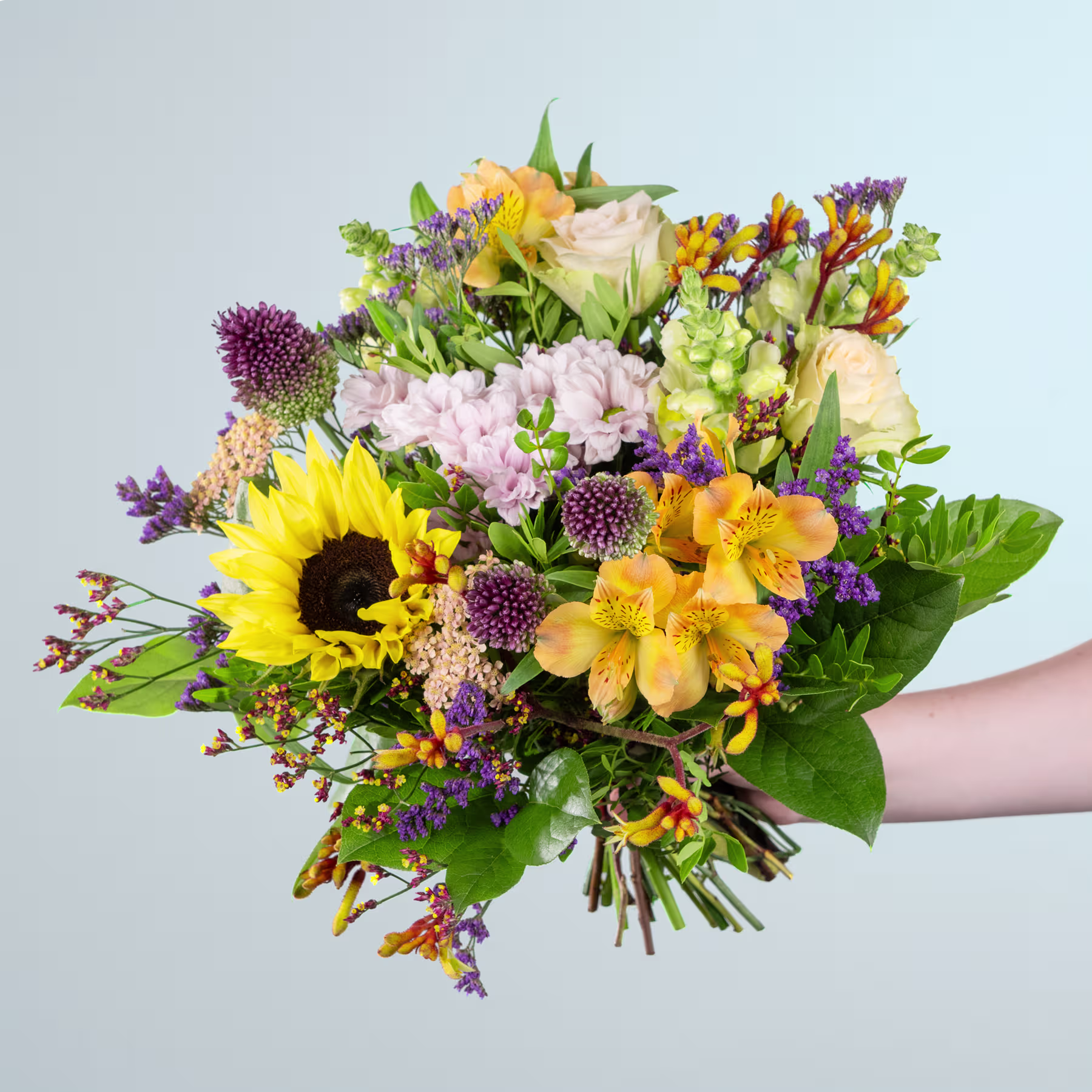 Ein leuchtender Strauß bunter Blumen, darunter Sonnenblumen, Dahlien und verschiedene andere Blüten, den eine Person vor einem schlichten Hintergrund in den Händen hält. (Beschreibungstext KI-generiert)