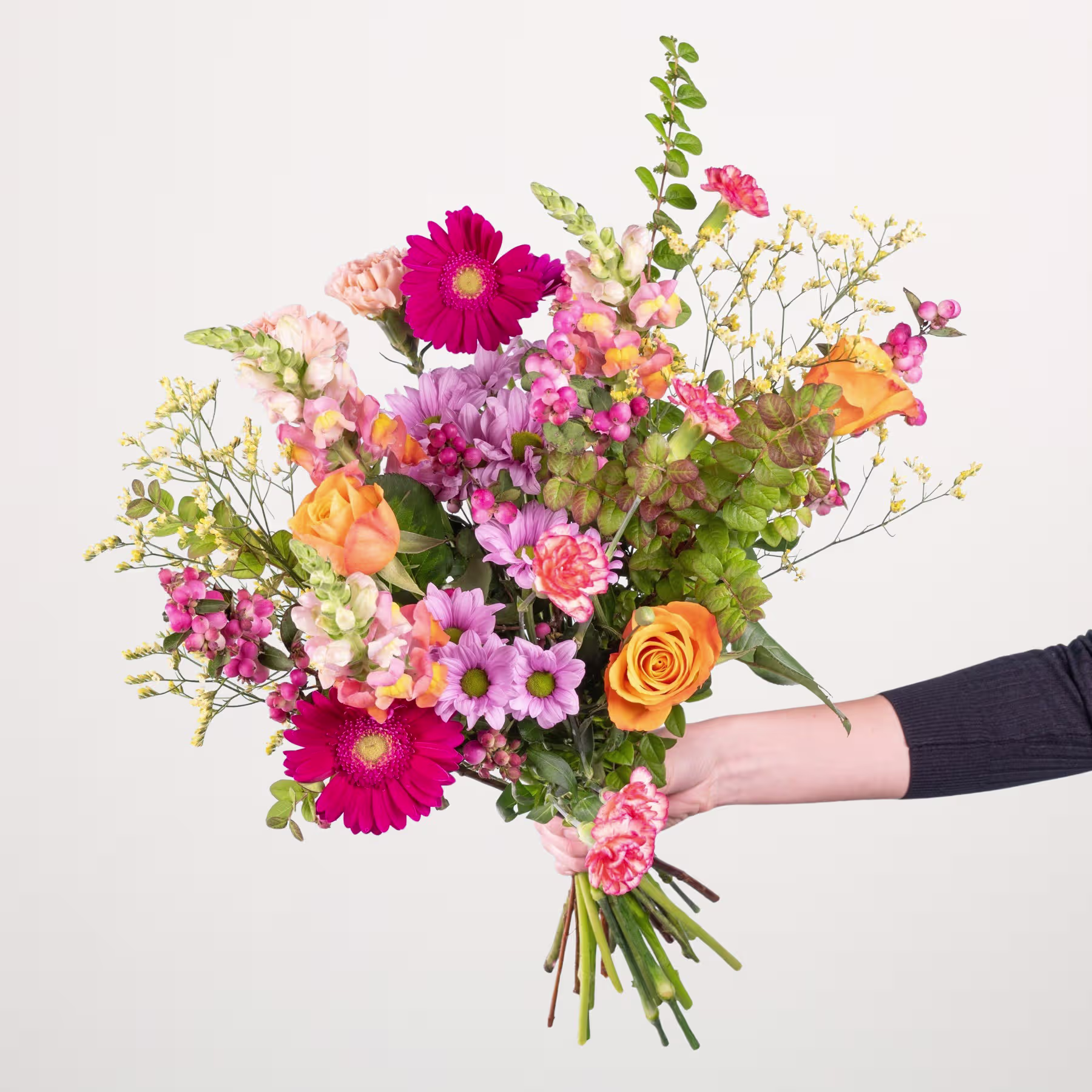 Ein leuchtender Strauß bunter Blumen, darunter rosa und orangefarbene Gerbera, Rosen und andere Blüten, die eine Person vor einem schlichten weißen Hintergrund in den Händen hält. (Beschreibungstext KI-generiert)