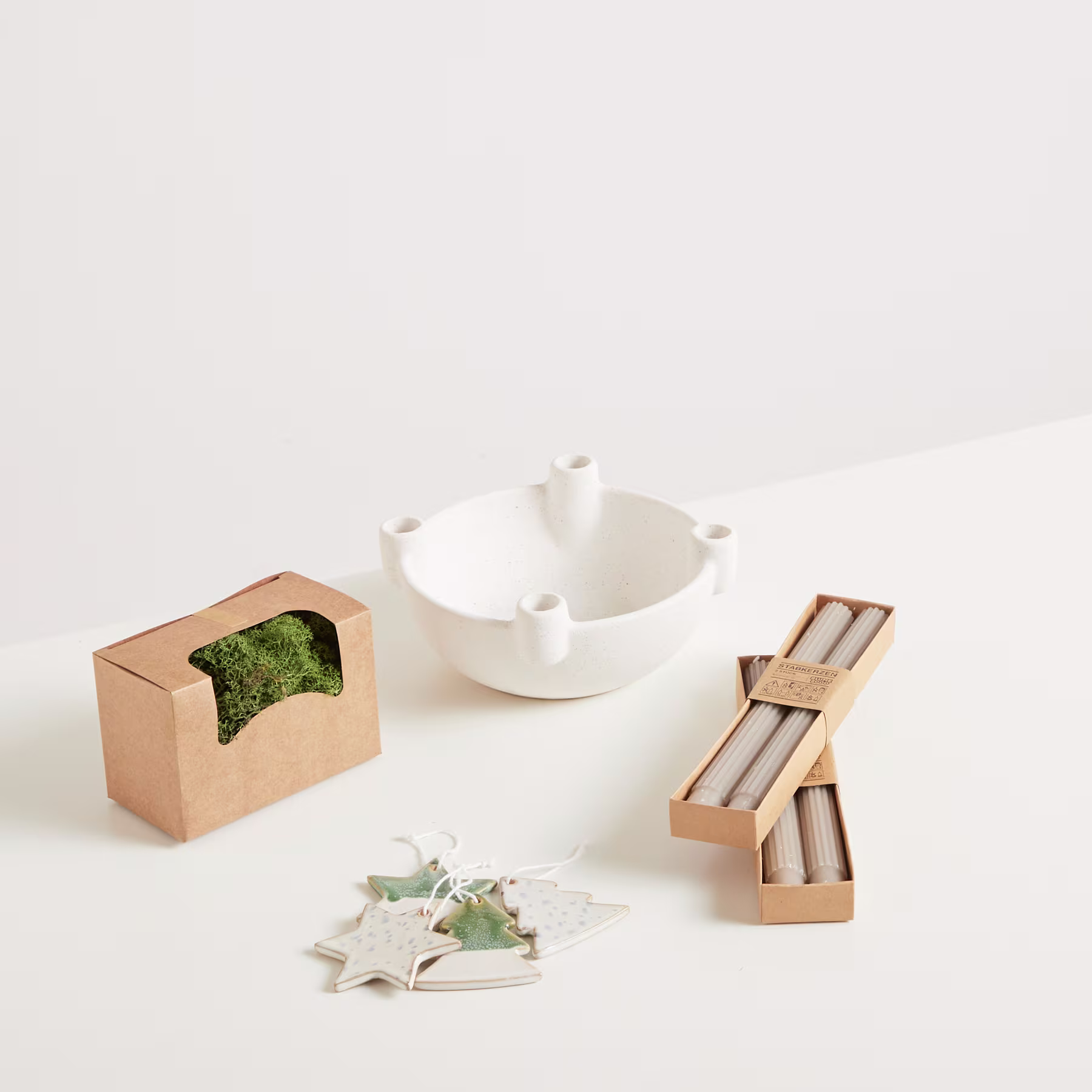 Eine weiße Teekanne aus Keramik, eine Holzkiste mit etwas, das wie Moos aussieht, und zwei Holzobjekte, die Essstäbchen oder Besteck ähneln, sind auf einem schlichten weißen Hintergrund angeordnet. (Beschreibungstext KI-generiert)