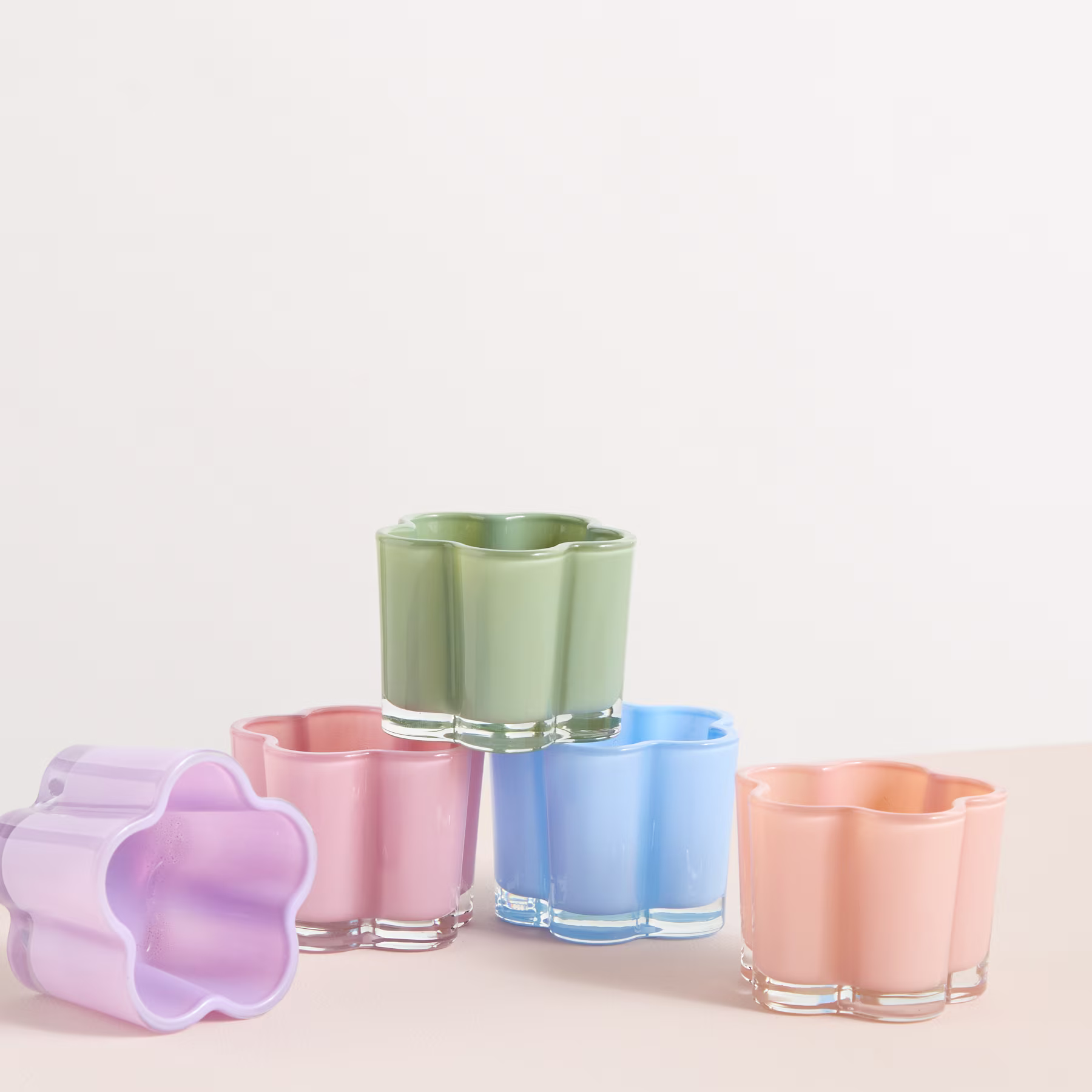 Eine Sammlung farbenfroher, blumenförmiger Glasbehälter in Pastelltönen von Grün, Rosa, Blau und Pfirsich, angeordnet auf einem schlichten weißen Hintergrund. (Beschreibungstext KI-generiert)