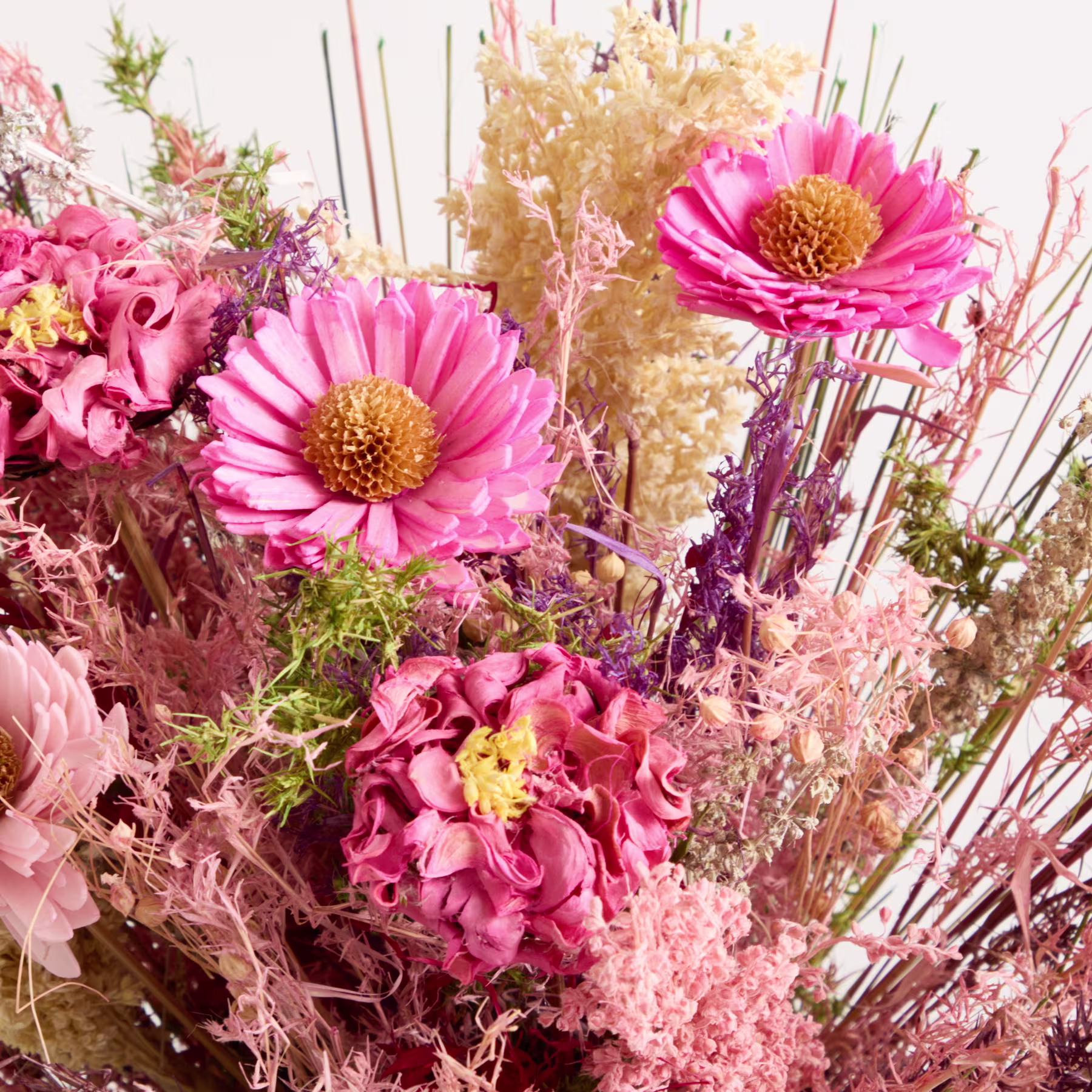 Ein lebendiger Strauß rosa und gelber Blumen, darunter Gerbera und Hortensien, vor einem Hintergrund aus getrockneten Blumenelementen und Grünpflanzen. (Beschreibungstext KI-generiert)