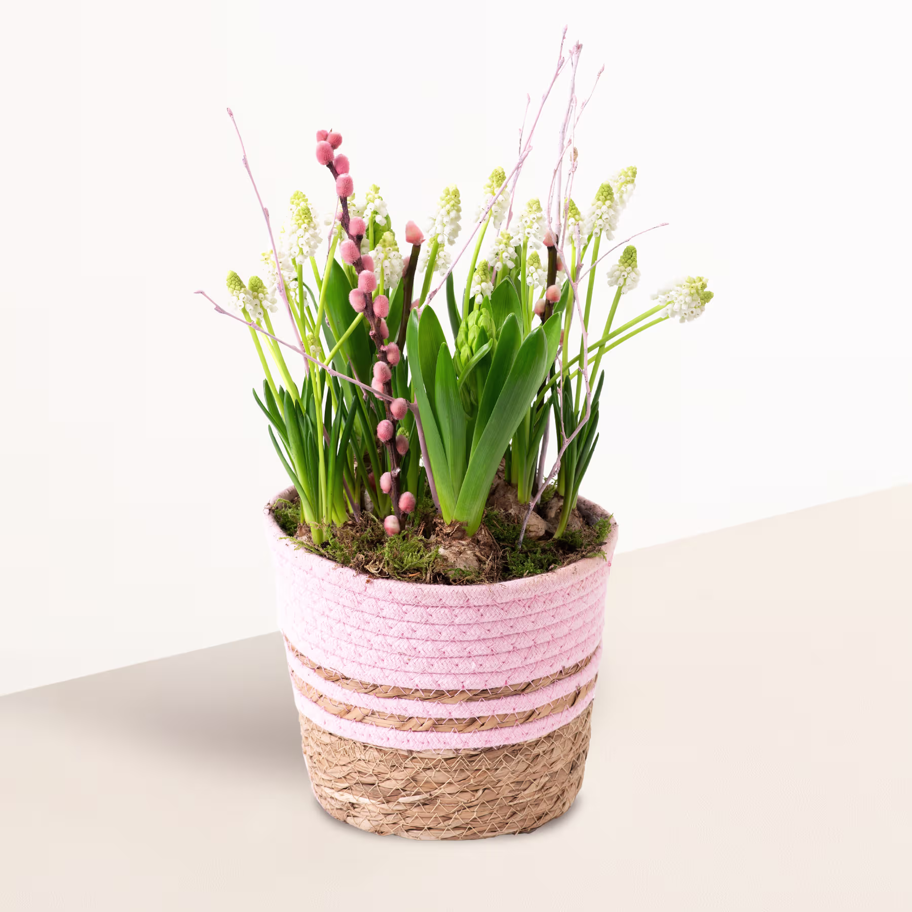 Ein lebendiges Arrangement aus rosa und grünen Pflanzen, darunter kleine Blumen und üppiges Laub, eingebettet in einen geflochtenen Korb mit Streifenmuster. (Beschreibungstext KI-generiert)