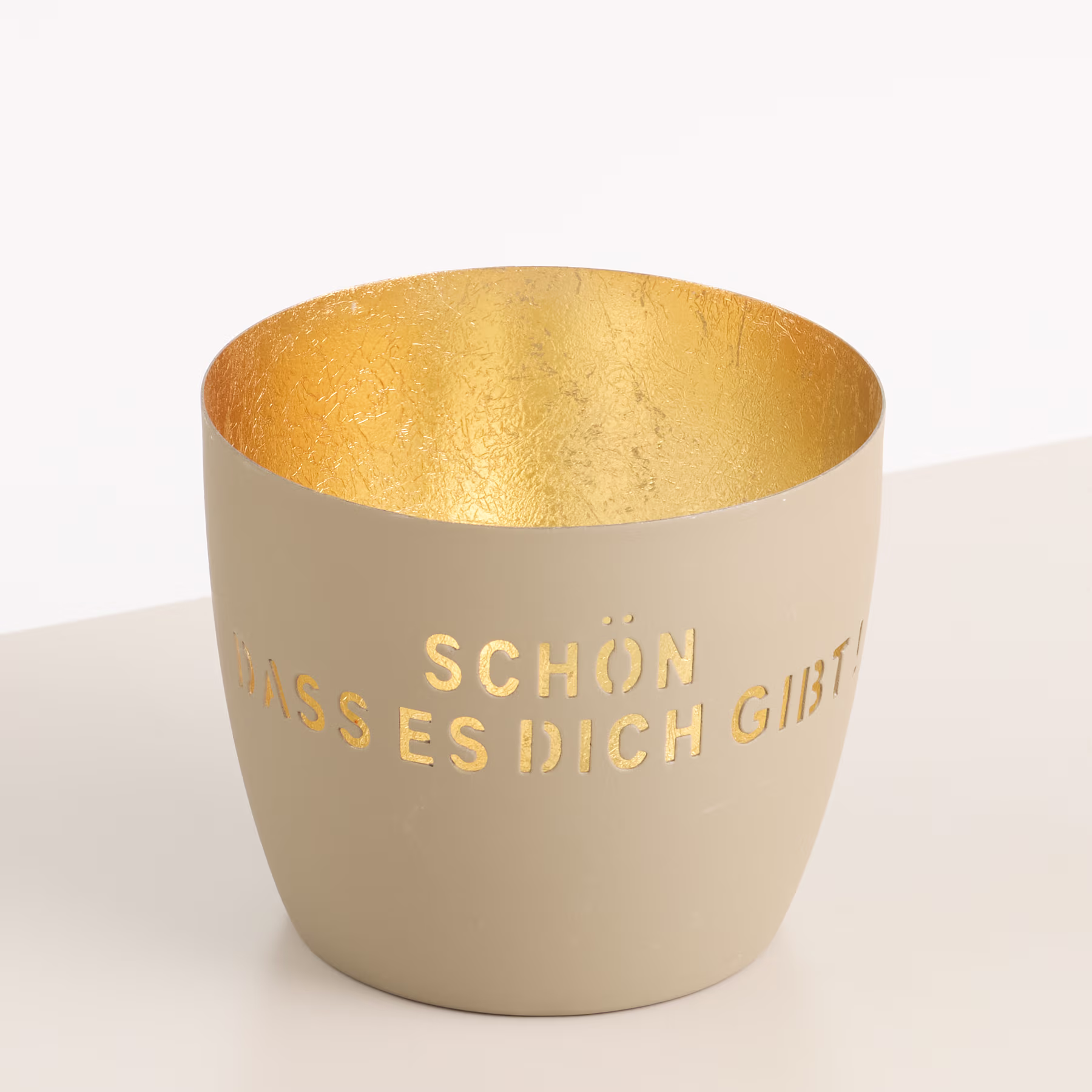 Eine beige Keramiktasse mit goldener Innenseite und dem in goldener Schrift aufgedruckten Text „Schon, dass es dich gibt“ auf der Außenseite. (Beschreibungstext KI-generiert)