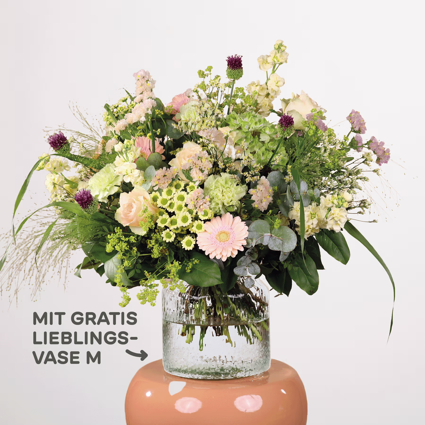 Ein farbenfroher Strauß verschiedener Blumen, darunter Chrysanthemen, Gänseblümchen und Grünpflanzen, wird in einer Glasvase auf einem Sockel präsentiert, mit einem Schild, das auf ein Sonderangebot für eine „Lieblingsvase“ hinweist. (Beschreibungstext KI-generiert)