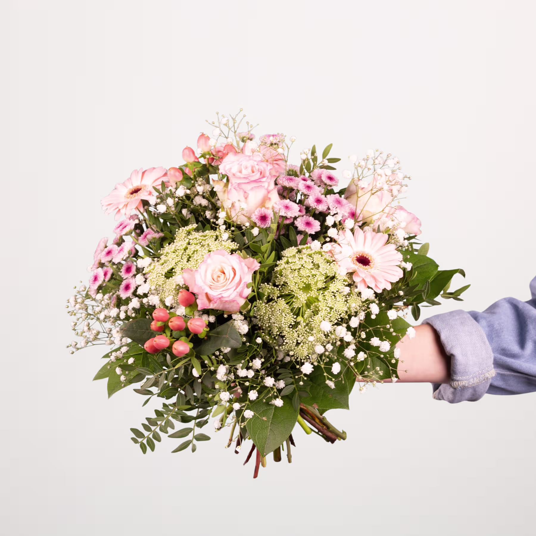 Ein leuchtender Strauß aus rosa Rosen, weißen Gänseblümchen und Grünpflanzen, der vor einem sanften blauen Hintergrund in den Händen einer Person gehalten wird. (Beschreibungstext KI-generiert)