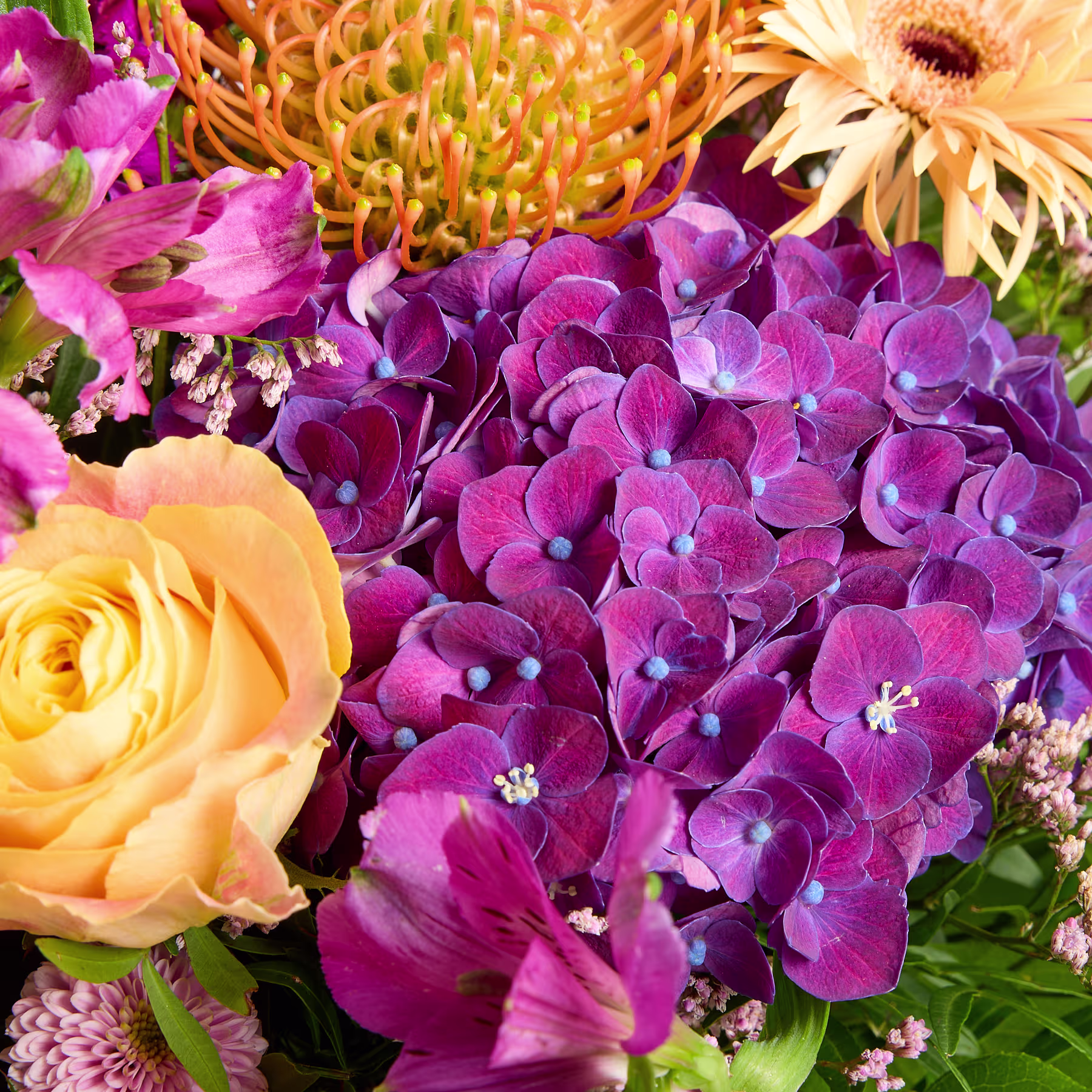 Ein lebendiger Strauß bunter Blumen, darunter rosa Hortensien, gelbe Rosen und eine große Sonnenblume, vor einem üppigen grünen Hintergrund. (Beschreibungstext KI-generiert)