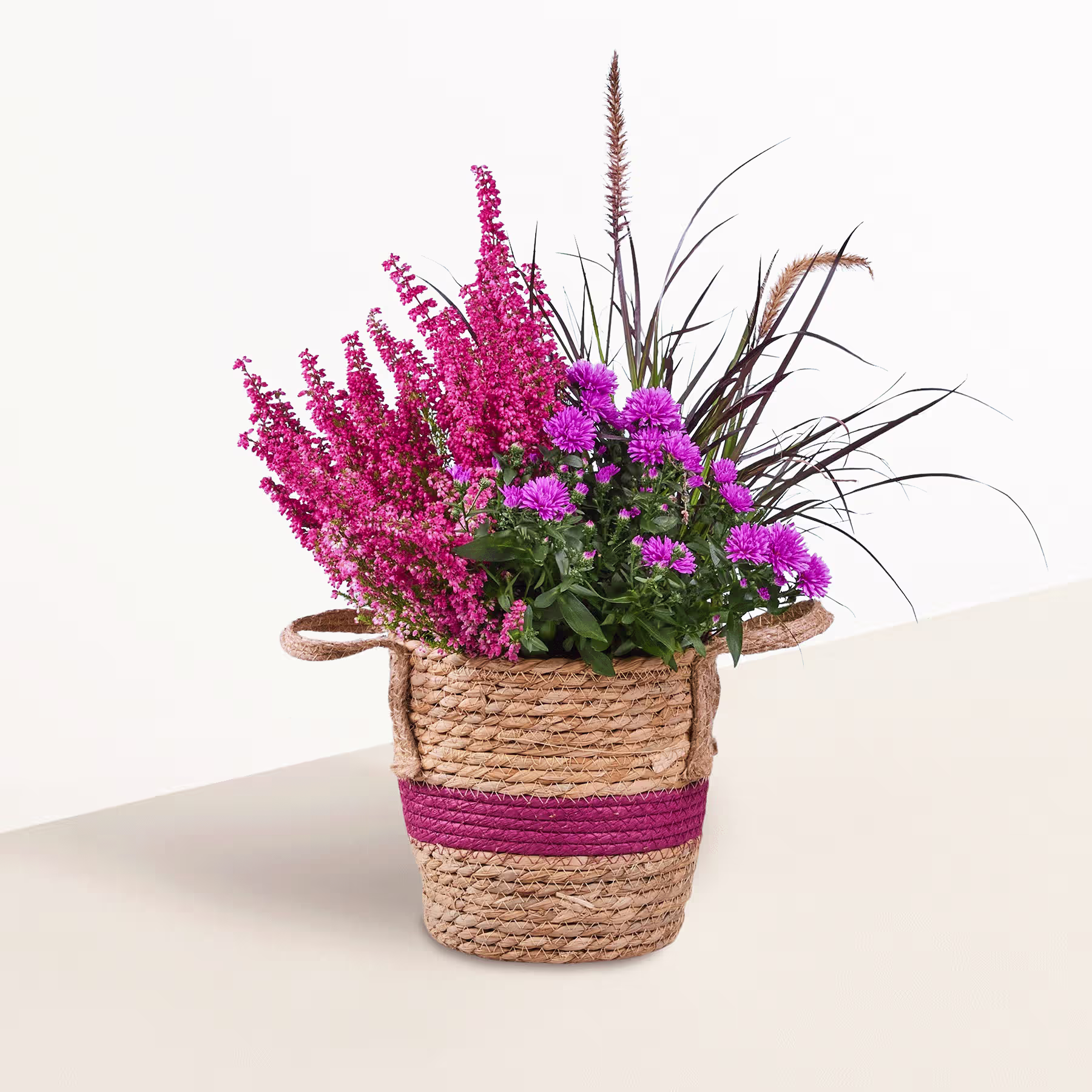 Ein geflochtener Korb voller leuchtend rosa und violetter Blumen vor einem hellblauen Hintergrund. (Beschreibungstext KI-generiert)