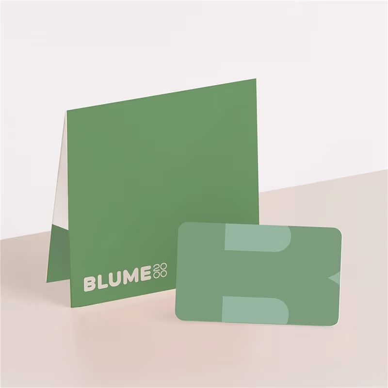 Auf einer hellen Unterlage liegen eine grüne Karte und eine grüne Mappe mit der Aufschrift „BLUME 88“. (Beschreibungstext KI-generiert)