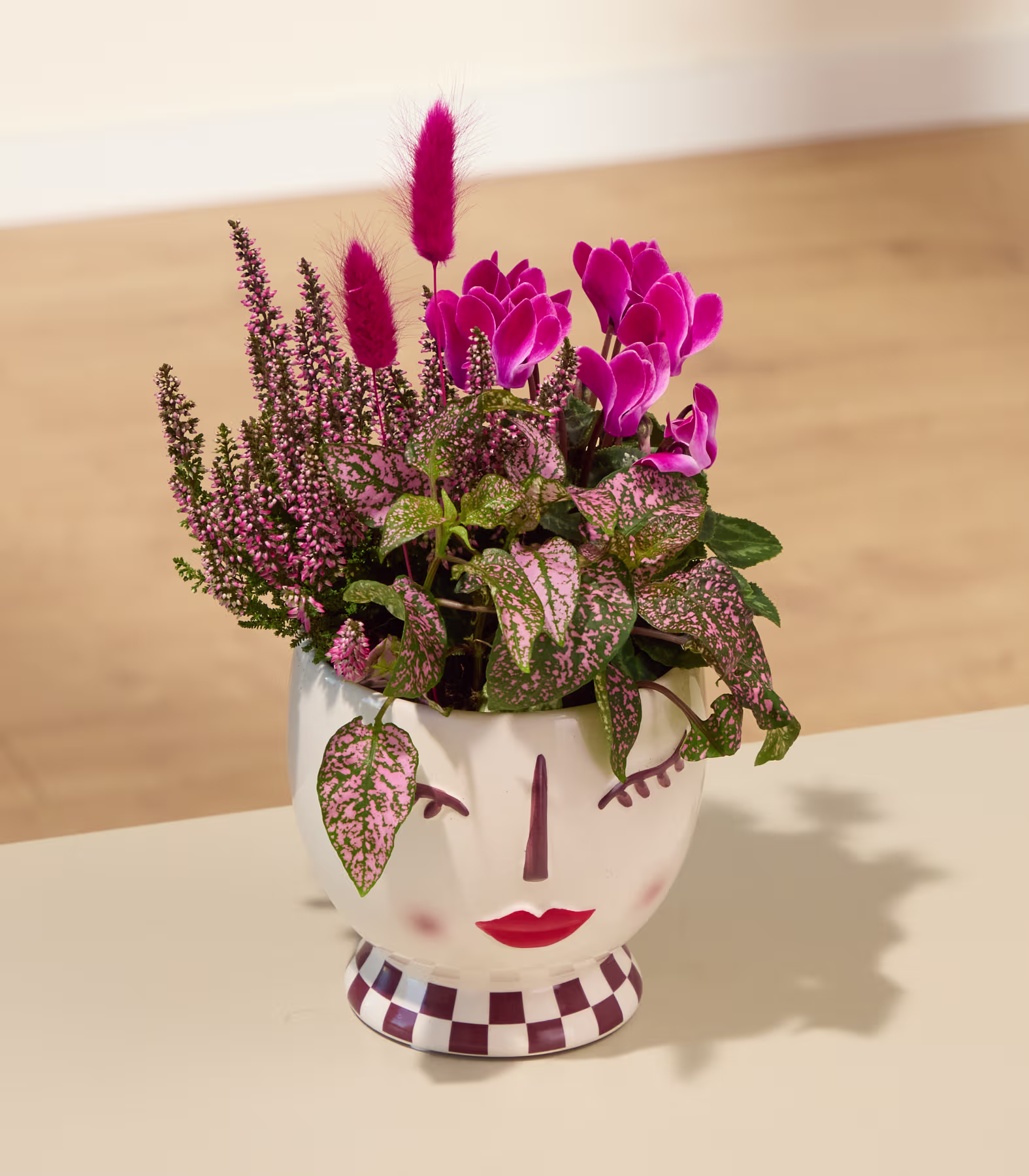 Ein lebendiger Strauß rosa Alpenveilchenblüten, umgeben von üppigem grünem Laub und zarten rosa Heideblüten, vor einem schlichten Hintergrund. (Beschreibungstext KI-generiert)