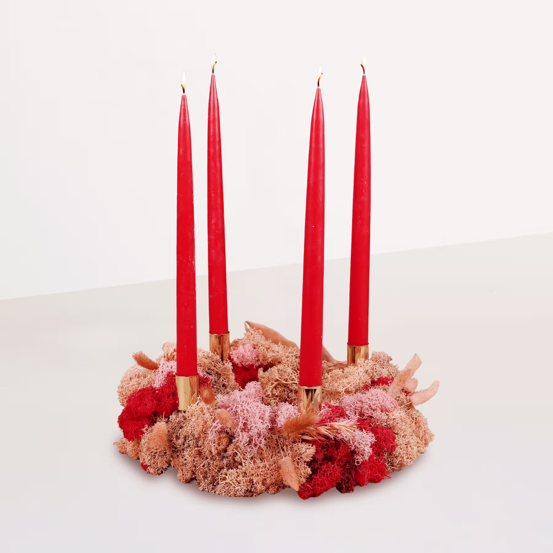 Auf einer Holzoberfläche steht ein kranzartiges Arrangement aus roten Kerzen, umgeben von rosa und roten Blumenelementen. (Beschreibungstext KI-generiert)