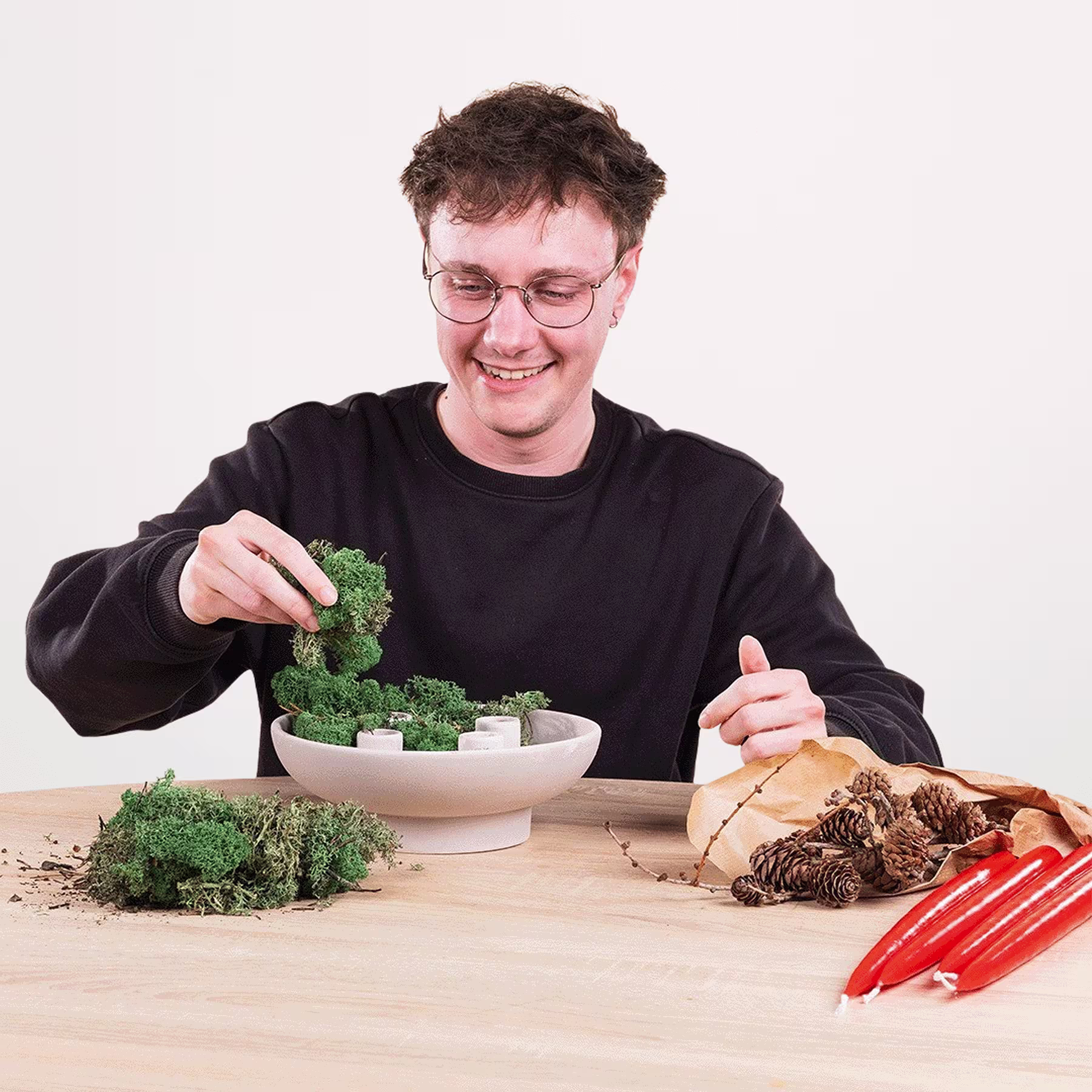 Eine Person in einem schwarzen Hemd arrangiert Brokkolistücke auf einem Holztisch, umgeben von verschiedenen anderen Lebensmitteln. (Beschreibungstext KI-generiert)
