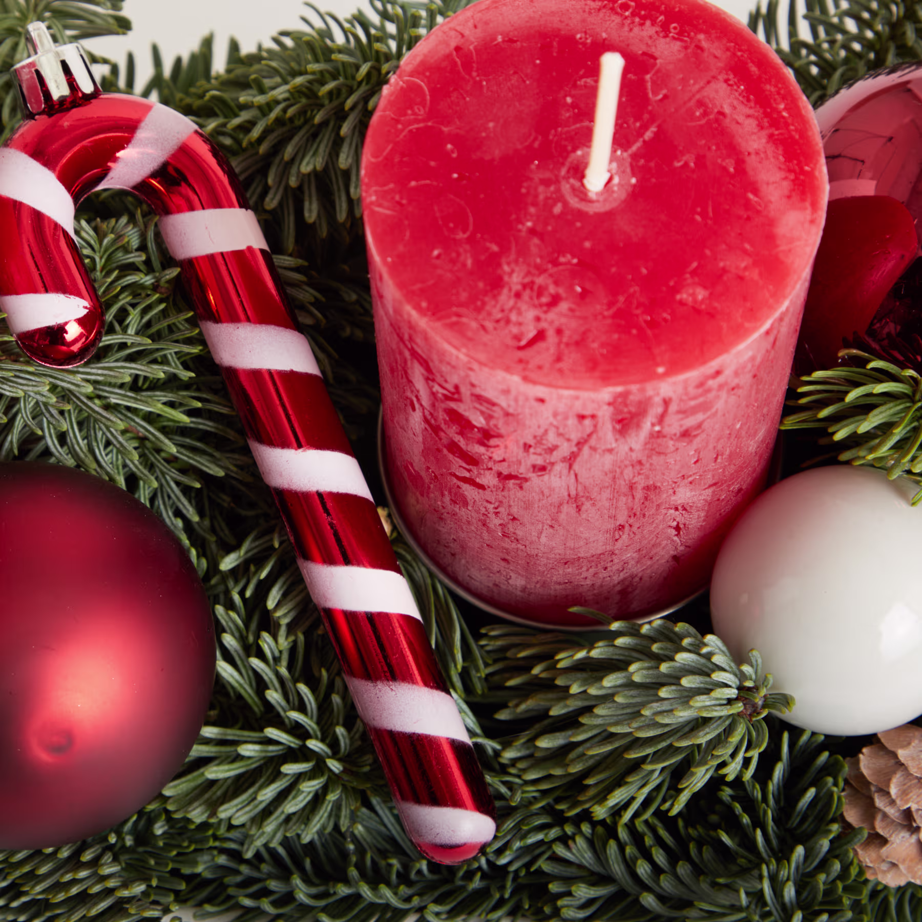 Eine leuchtend rote Kerze, umgeben von festlicher Weihnachtsdekoration, darunter Zuckerstangen, Ornamente und immergrüne Zweige, schafft eine gemütliche und weihnachtliche Szene. (Beschreibungstext KI-generiert)