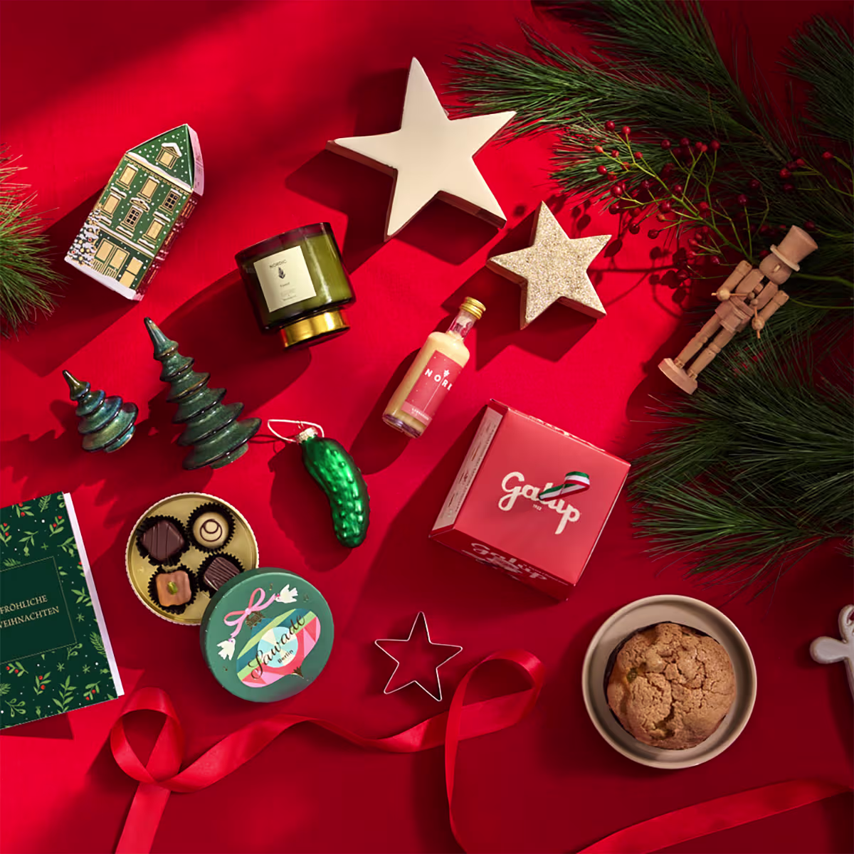 Ein festliches Arrangement aus Weihnachtsdekorationen, darunter ein Stern, Ornamente, eine Kerze und eine Schüssel mit Keksen, vor einem leuchtend roten Hintergrund. (Beschreibungstext KI-generiert)