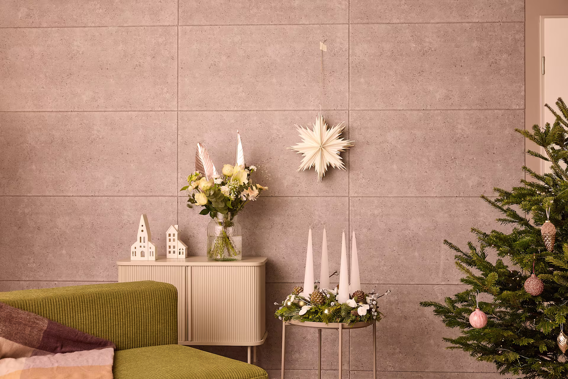 Ein gemütliches Wohnzimmer mit einem geschmückten Weihnachtsbaum, einer Vase mit Blumen und verschiedenen Deko-Elementen auf einem Schrank im Vordergrund. (Beschreibungstext KI-generiert)