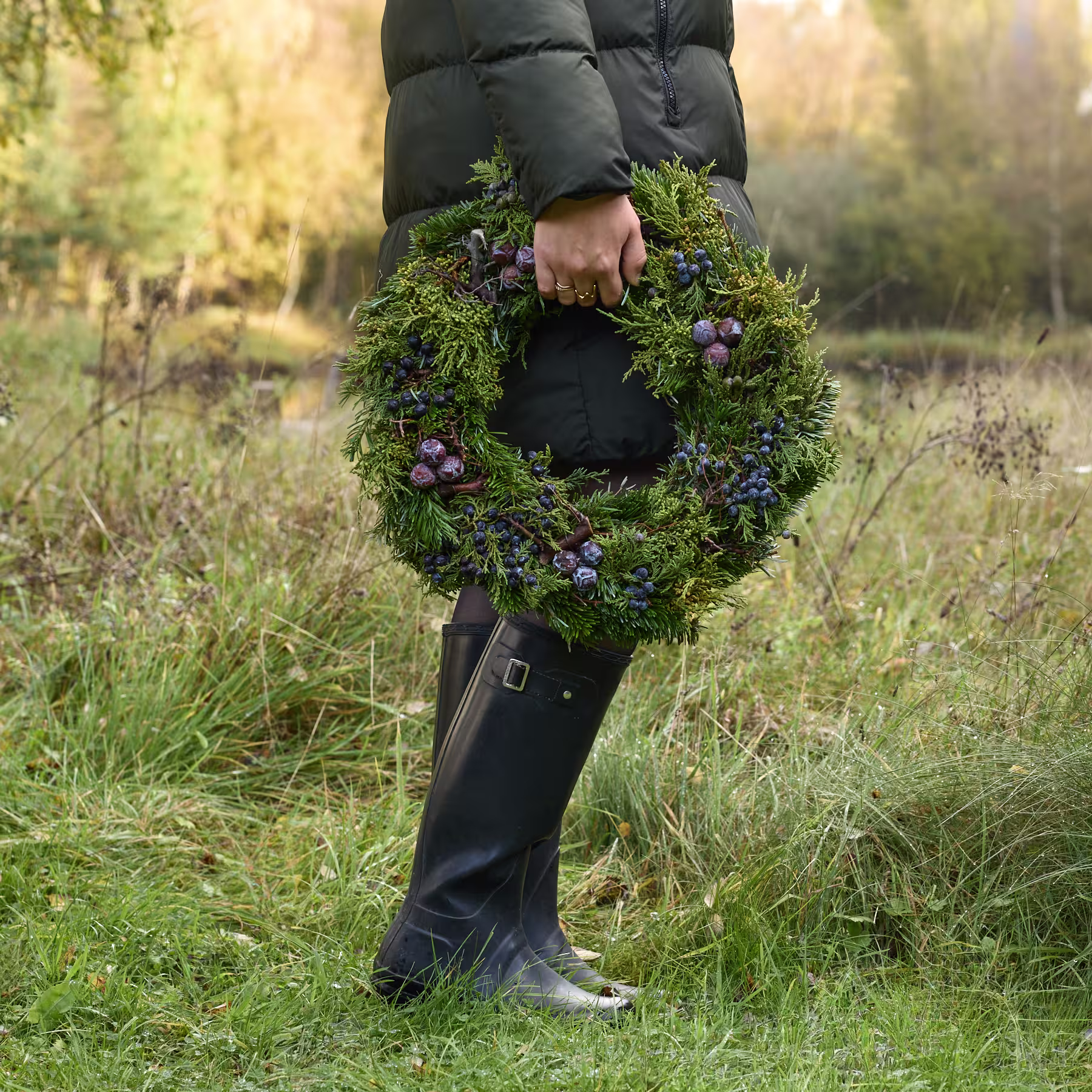 Ein üppiger, moosbedeckter Kranz, geschmückt mit Büscheln violetter Beeren und Zweige, vor einem schlichten weißen Hintergrund. (Beschreibungstext KI-generiert)
