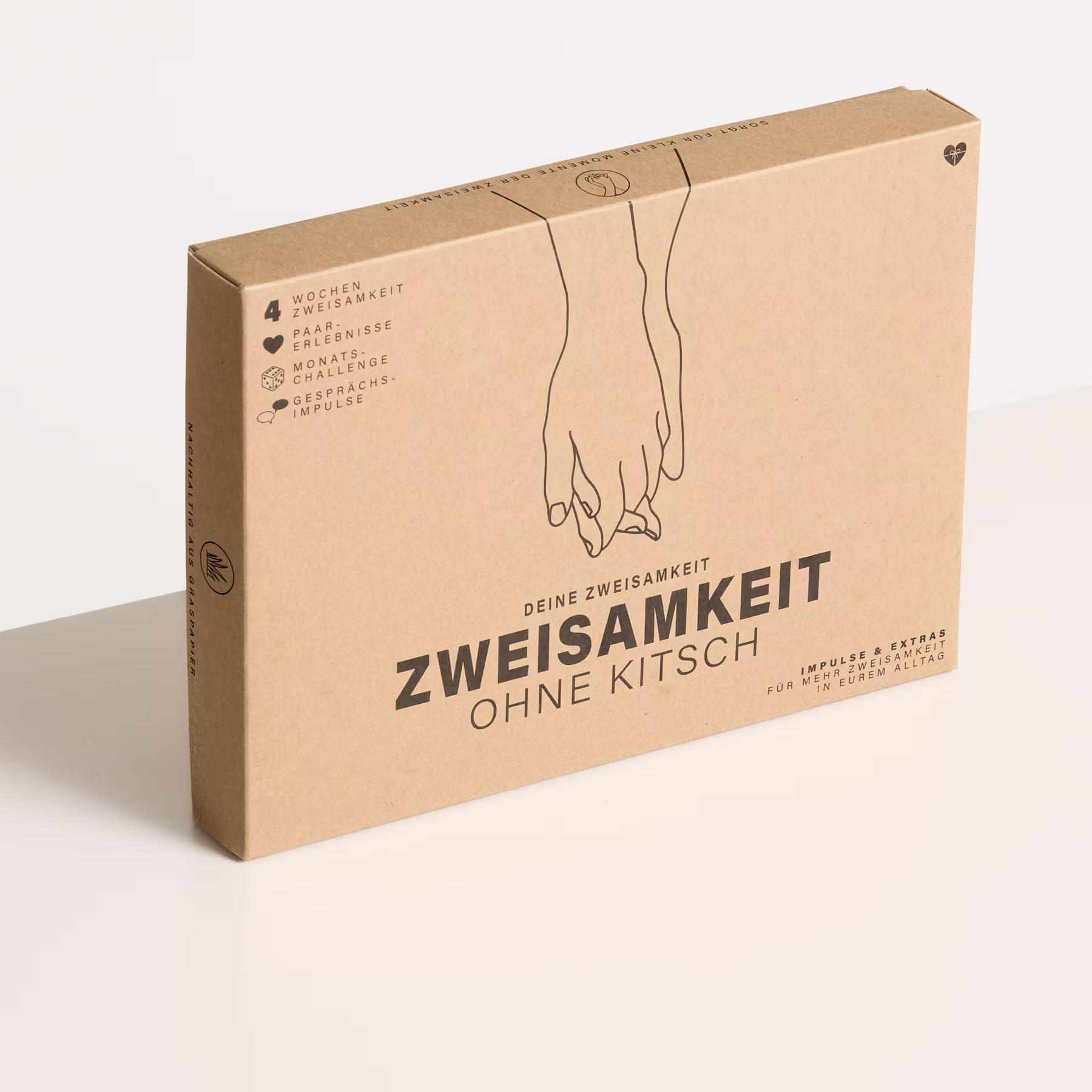 Ein Karton mit dem Aufdruck „Zweisamkeit ohne Kitsch“ auf schlichtem weißem Hintergrund. (Beschreibungstext KI-generiert)