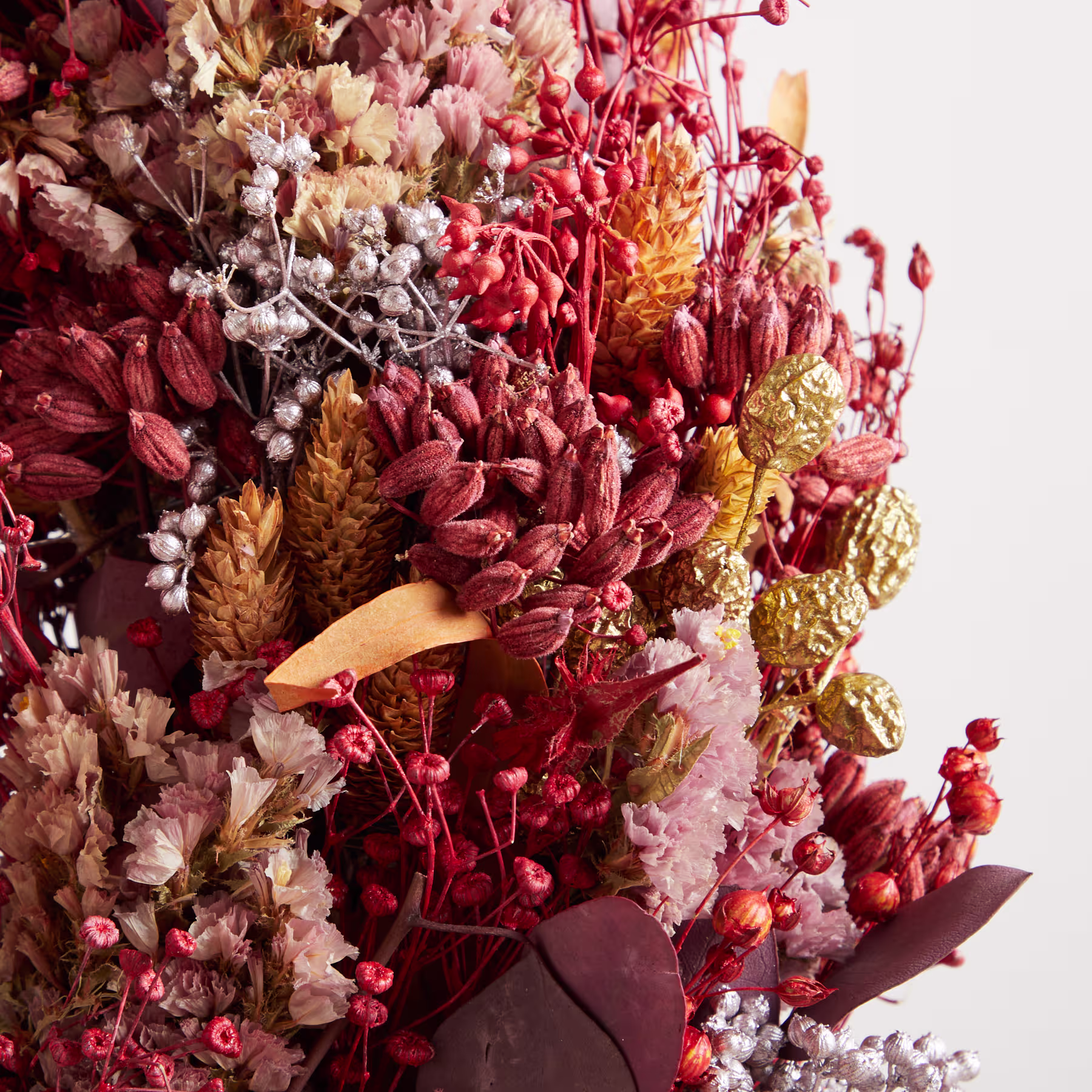 Ein lebhafter Blumenstrauß aus roten, rosa und gelben Blumen, darunter Chrysanthemen und andere Blüten, füllt das Bildfeld vor einem schlichten weißen Hintergrund. (Beschreibungstext KI-generiert)