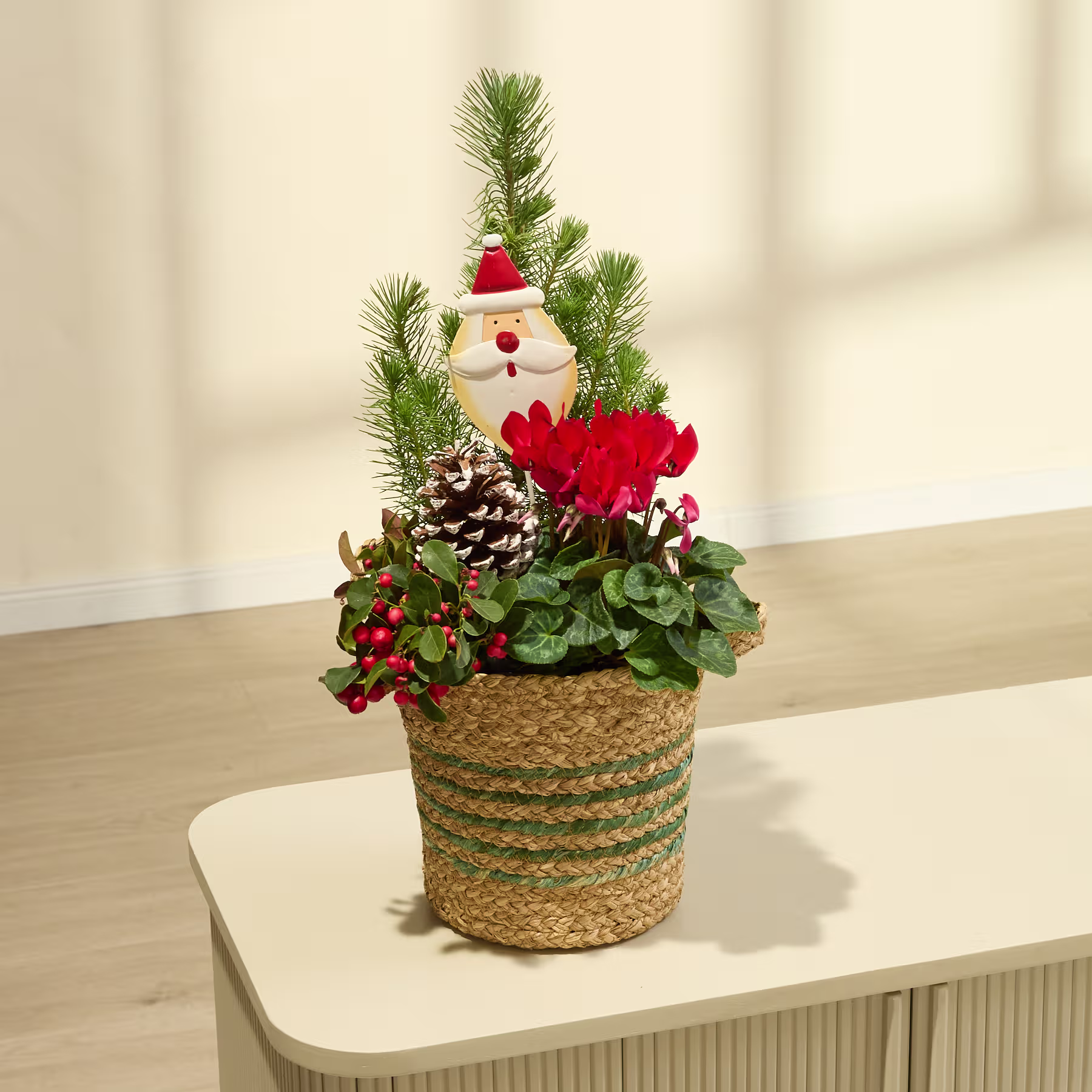 Ein festliches Weihnachtsarrangement mit einer kleinen Schneemannfigur, Kiefernzweigen, roten Weihnachtssternen und einem geflochtenen Korb auf einer Holzoberfläche. (Beschreibungstext KI-generiert)