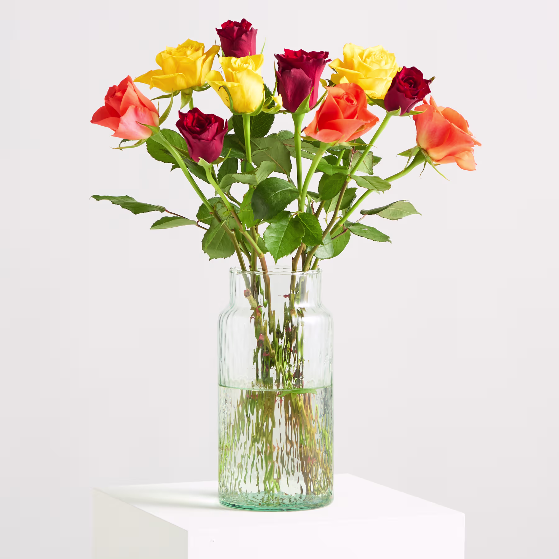 Ein lebendiger Strauß farbenfroher Rosen, darunter tiefrote, leuchtend gelbe und leuchtend orange Blüten, vor einem weichen, unscharfen Hintergrund. (Beschreibungstext KI-generiert)