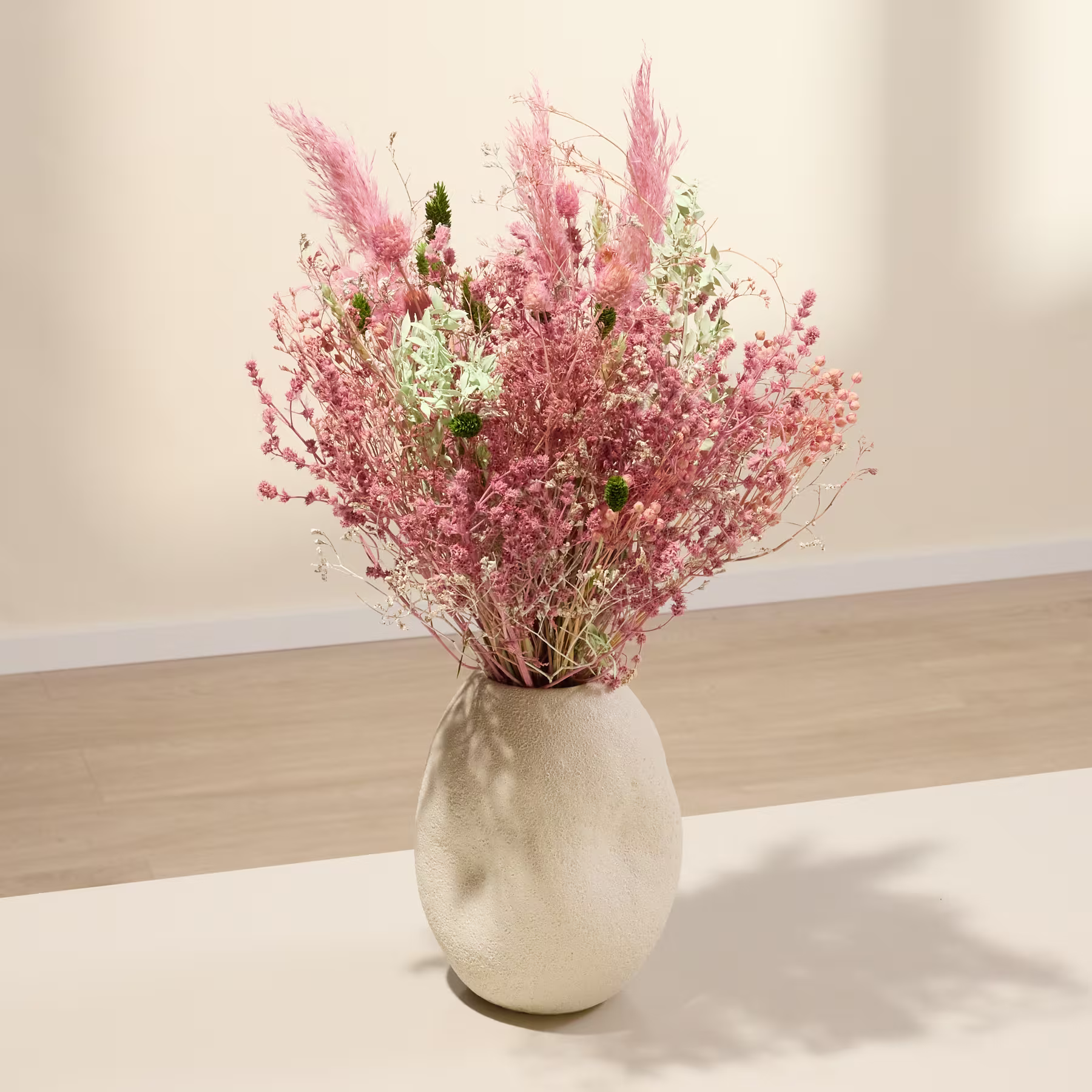 Eine Vase, gefüllt mit einem farbenfrohen Strauß aus rosa und weißen Trockenblumen, steht auf einer Holzoberfläche vor einem schlichten Hintergrund. (Beschreibungstext KI-generiert)