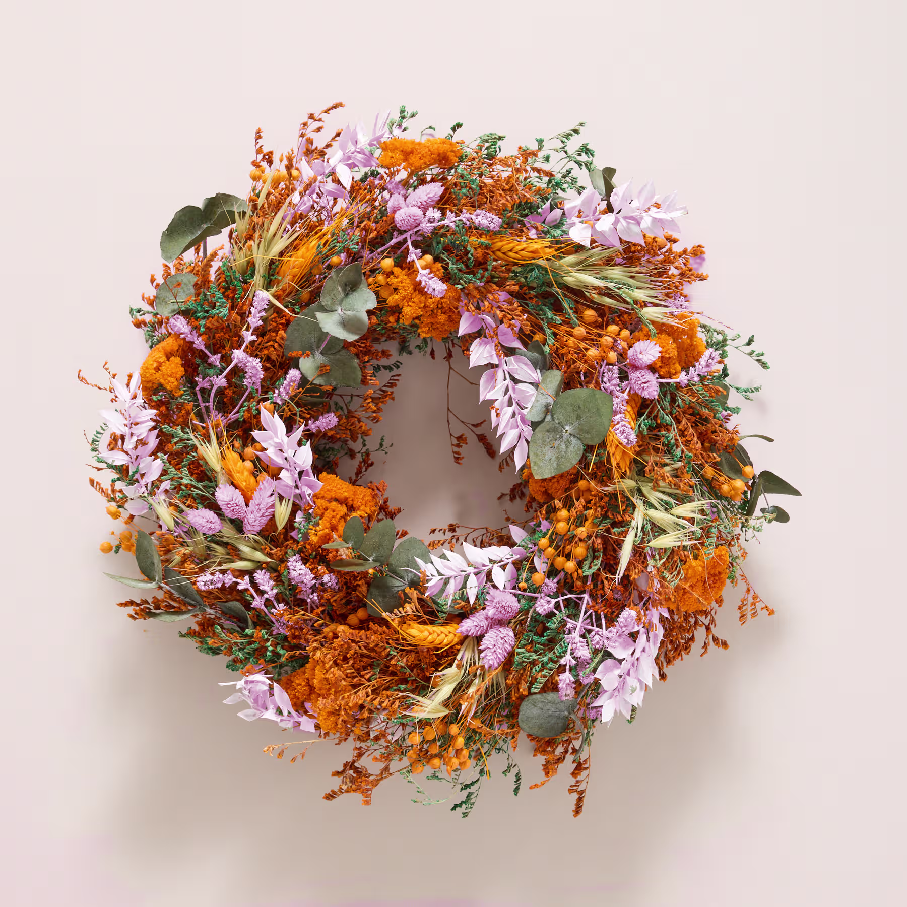 Ein lebendiger und farbenfroher Kranz aus verschiedenen getrockneten Blumen, Blättern und anderen natürlichen Elementen, präsentiert vor einem schlichten weißen Hintergrund. (Beschreibungstext KI-generiert)