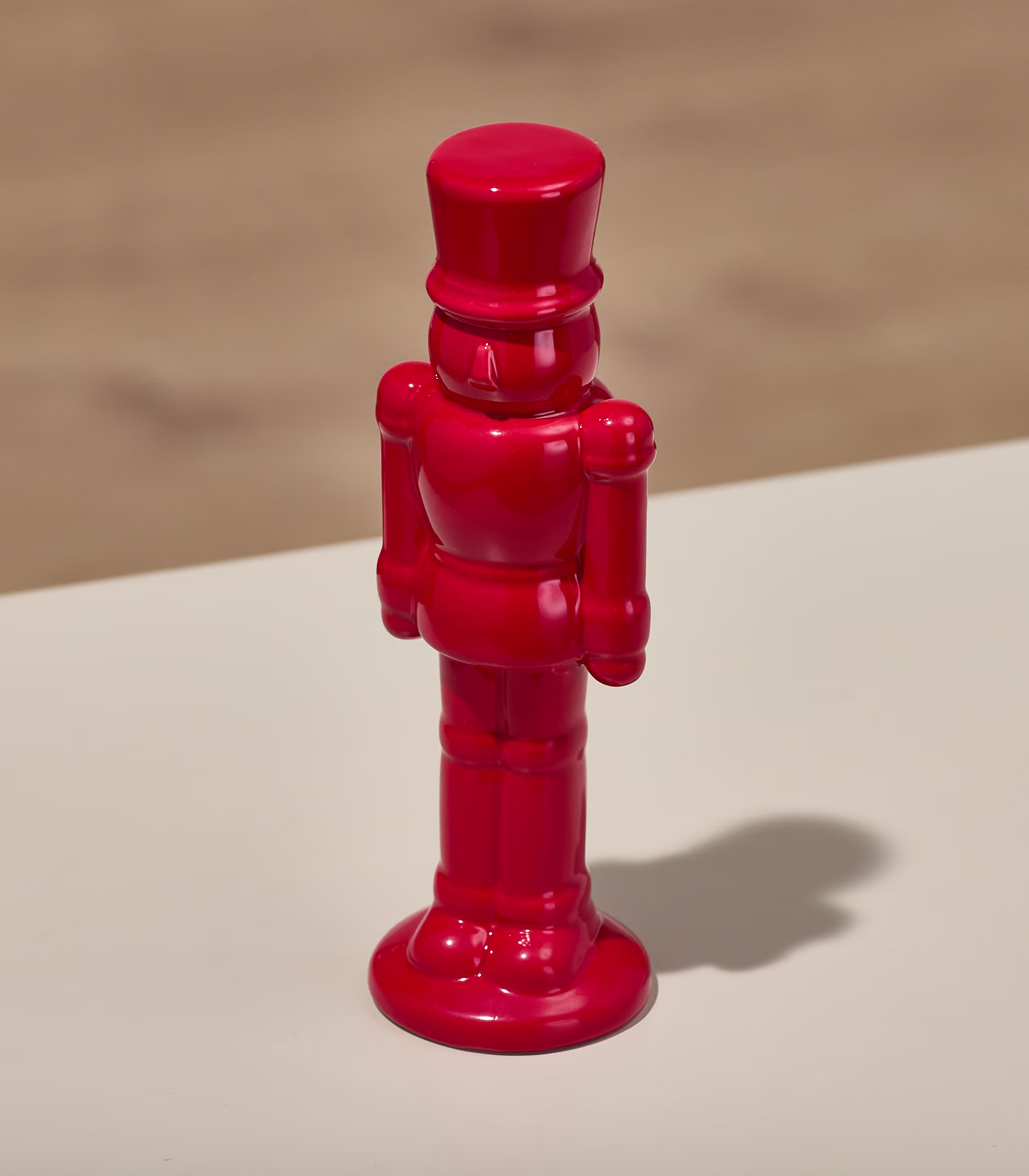 Eine leuchtend rote Nussknackerfigur aus Holz steht auf einer hellen Oberfläche; ihre filigranen Details und die kräftige Farbe bilden einen Kontrast zum schlichten Hintergrund. (Beschreibungstext KI-generiert)