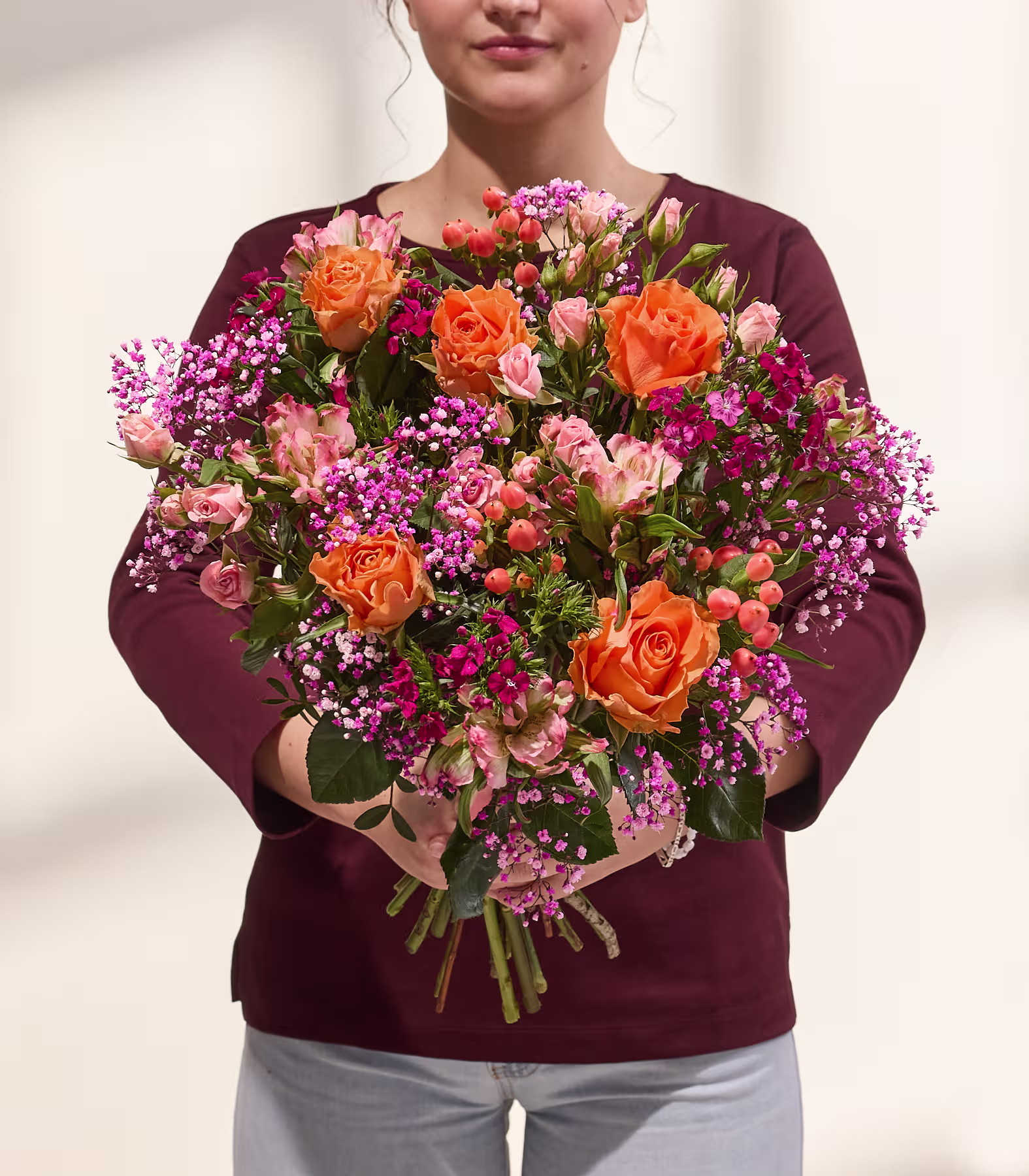 Ein farbenfroher Blumenstrauß mit Rosen, Dahlien und anderen Blüten wird von einer Person in einem schwarzen Hemd vor einem schlichten weißen Hintergrund gehalten. (Beschreibungstext KI-generiert)