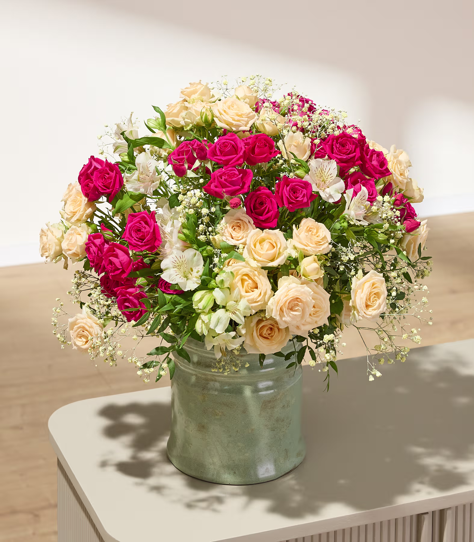 Ein farbenfroher Strauß verschiedener Blumen, darunter rote Rosen, rosa Nelken und weiße Lilien, arrangiert in einer klaren Glasvase vor einem schlichten weißen Hintergrund. (Beschreibungstext KI-generiert)
