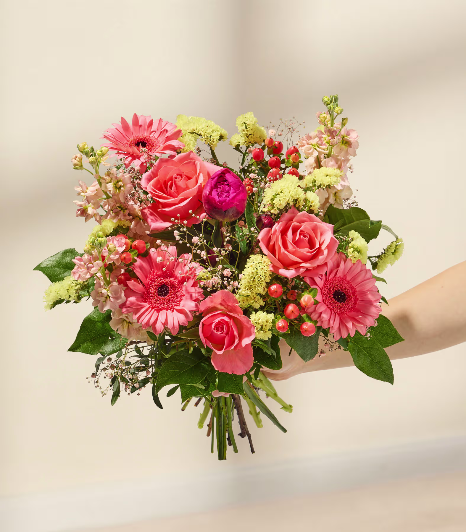 Ein lebhafter Strauß bunter Blumen, darunter rote Rosen, rosa Gerbera und grünes Laub, wird vor einem sanften, neutralen Hintergrund präsentiert. (Beschreibungstext KI-generiert)