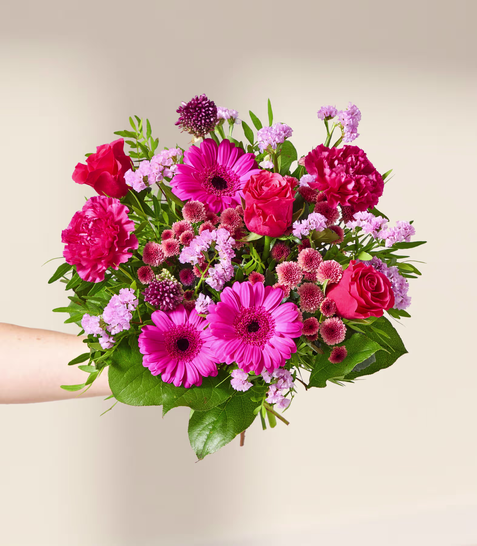 Eine Hand hält einen leuchtenden Strauß rosa und roter Blumen, darunter Gerbera und Rosen, vor einem sanften, neutralen Hintergrund. (Beschreibungstext KI-generiert)
