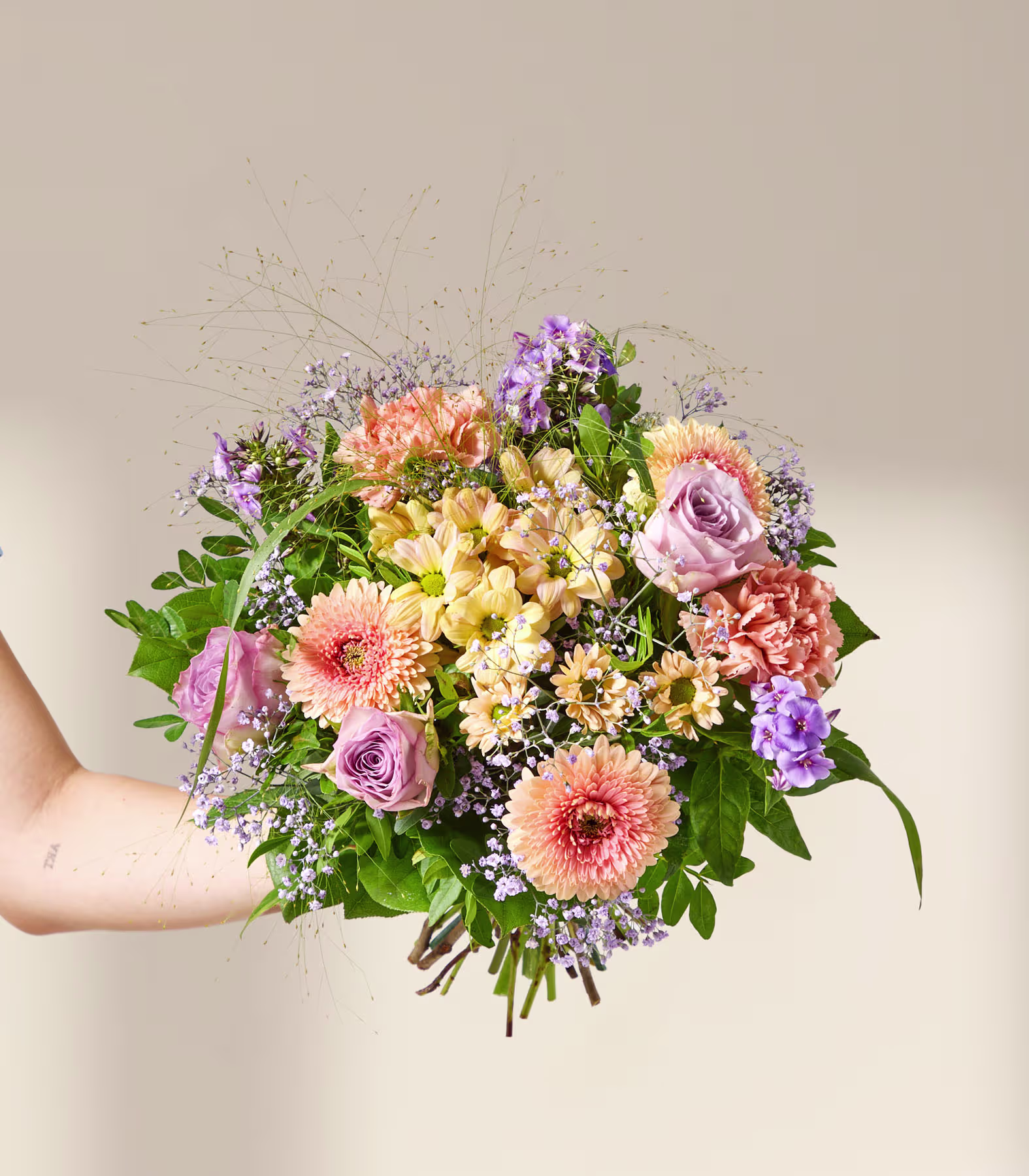 Im Vordergrund hält eine Person einen bunten Blumenstrauß am Arm; der Hintergrund ist sanft und neutral gehalten. (Beschreibungstext KI-generiert)