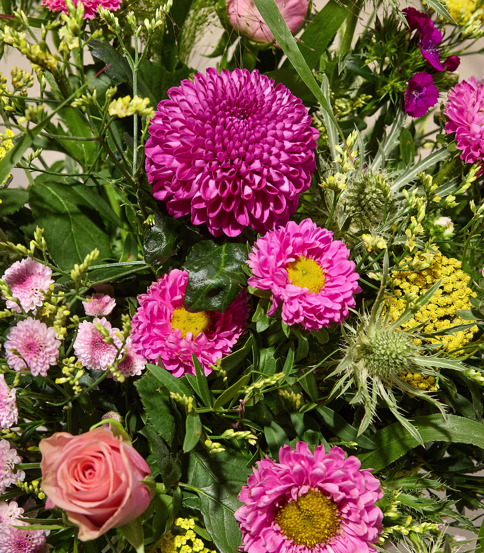 Ein leuchtender Strauß aus rosa und pfirsichfarbenen Blumen, darunter eine große Chrysantheme und Rosen, hebt sich von einem weichen, verschwommenen Hintergrund ab. (Beschreibungstext KI-generiert)