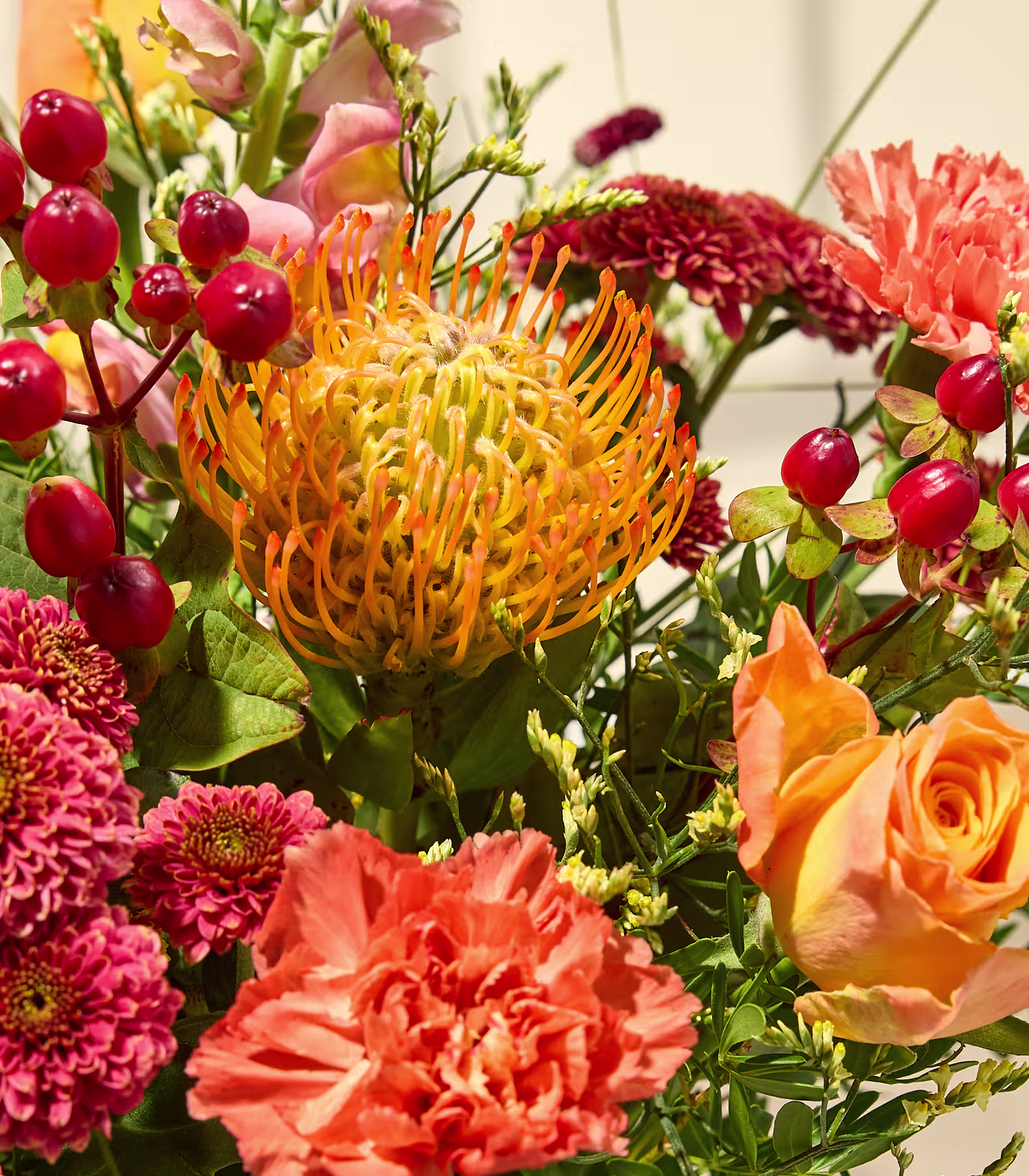 Im Vordergrund steht ein leuchtender Strauß orangefarbener und roter Blumen in einer Glasvase auf einem Holztisch; im sanft beleuchteten Hintergrund sind ein Sofa und eine Stehlampe zu sehen. (Beschreibungstext KI-generiert)