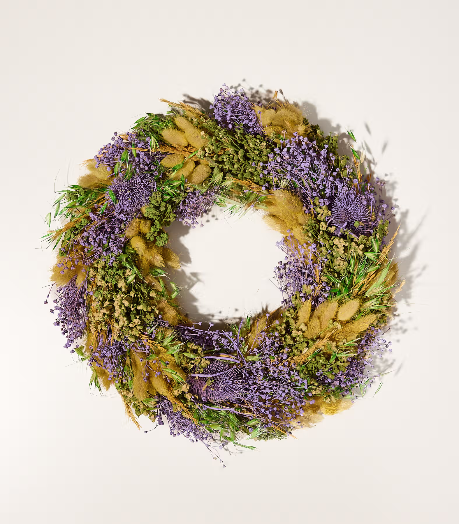 Ein rustikaler Kranz aus getrocknetem Lavendel, Gräsern und Grünzeug liegt auf einem schlichten weißen Hintergrund. (Beschreibungstext KI-generiert)
