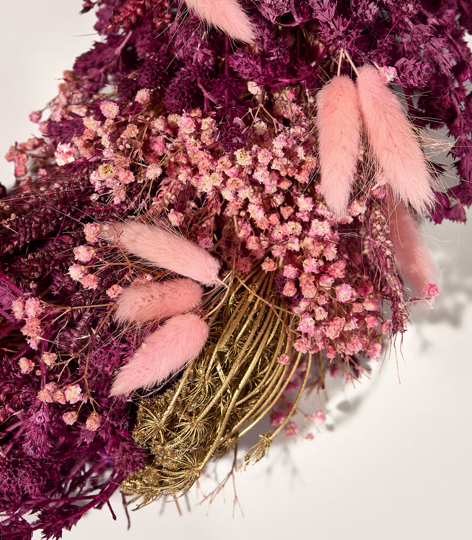 Eine Nahaufnahme eines Trockenblumenarrangements zeigt zartrosa Schleierkraut und flauschige rosa Hasenschwänze im Vordergrund vor einem Hintergrund aus tief burgunderrotem und goldenem Trockenlaub. (Beschreibungstext KI-generiert)