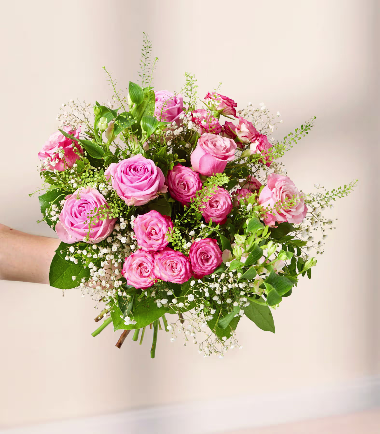 Ein üppiger Strauß aus rosa Rosen und anderen zarten Blumen liegt auf einer hellen Oberfläche, umgeben von einem weichen, verschwommenen Hintergrund. (Beschreibungstext KI-generiert)