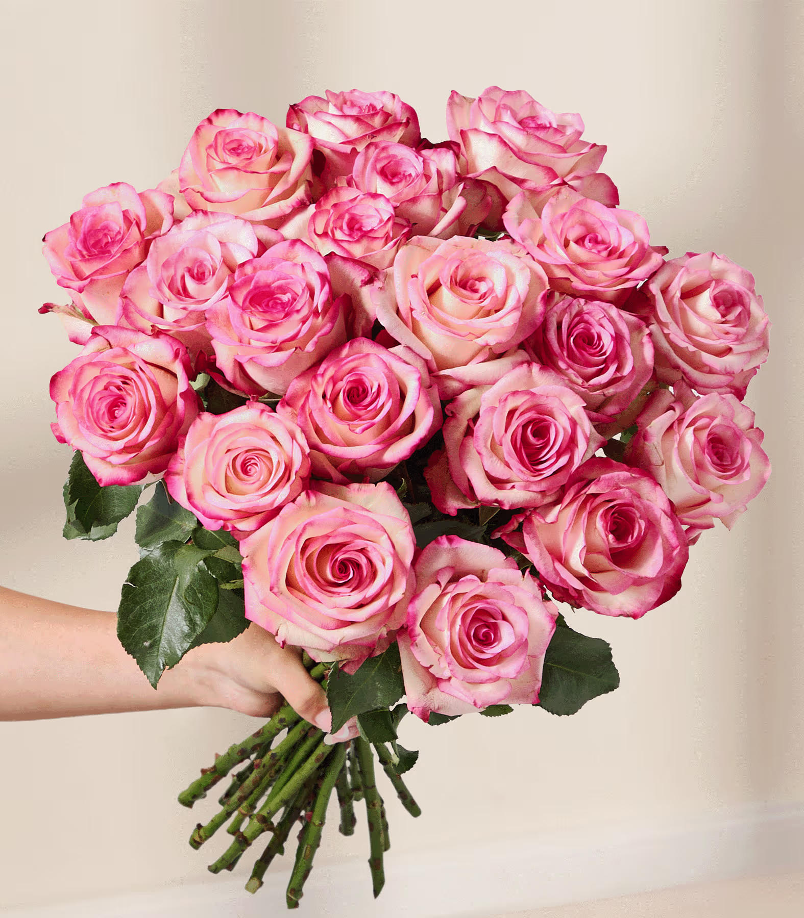 Ein wunderschöner Strauß leuchtend pinkfarbener Rosen in einer Glasvase steht auf einer hellen Fläche vor einer schlichten weißen Wand. (Beschreibungstext KI-generiert)