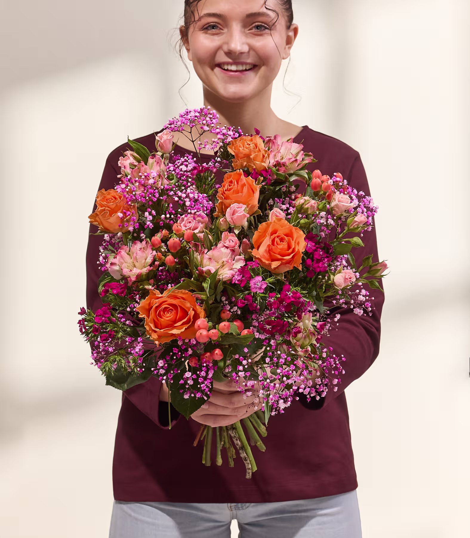Ein lebhafter Blumenstrauß aus roten, rosa und orangen Blüten, darunter Rosen, Alstroemerien und andere Blüten, füllt das Bild vor einem schlichten weißen Hintergrund. (Beschreibungstext KI-generiert)