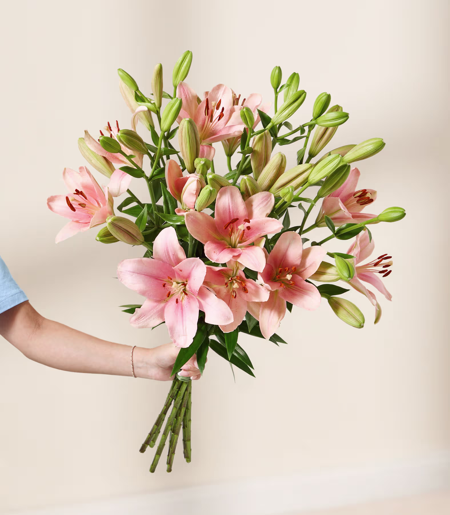 Eine junge Frau mit langen braunen Haaren hält vor einem schlichten weißen Hintergrund einen großen Strauß rosa Lilien. (Beschreibungstext KI-generiert)