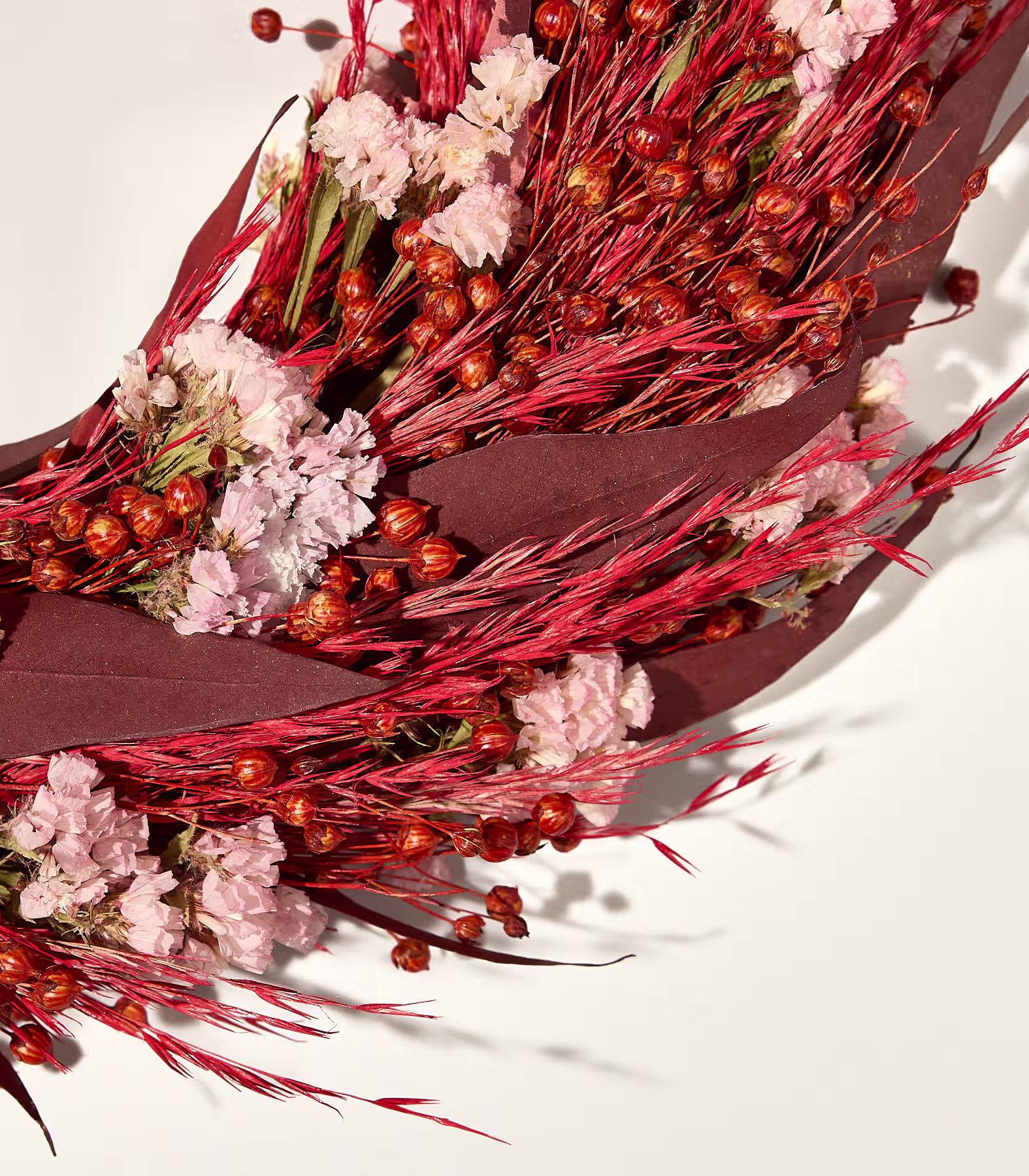 Ein in braunes Papier gewickelter Strauß getrockneter rosa Blüten und roter Beeren liegt vor einem schlichten weißen Hintergrund. (Beschreibungstext KI-generiert)