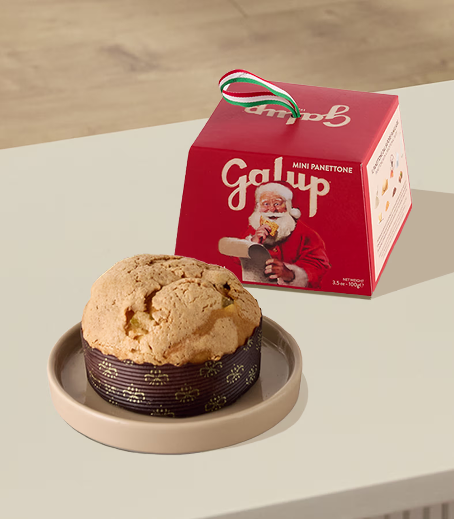 Neben einem Teller, auf dem ein großer, goldbrauner Keks auf einer weißen Oberfläche liegt, steht eine rote Galup-Schachtel. (Beschreibungstext KI-generiert)