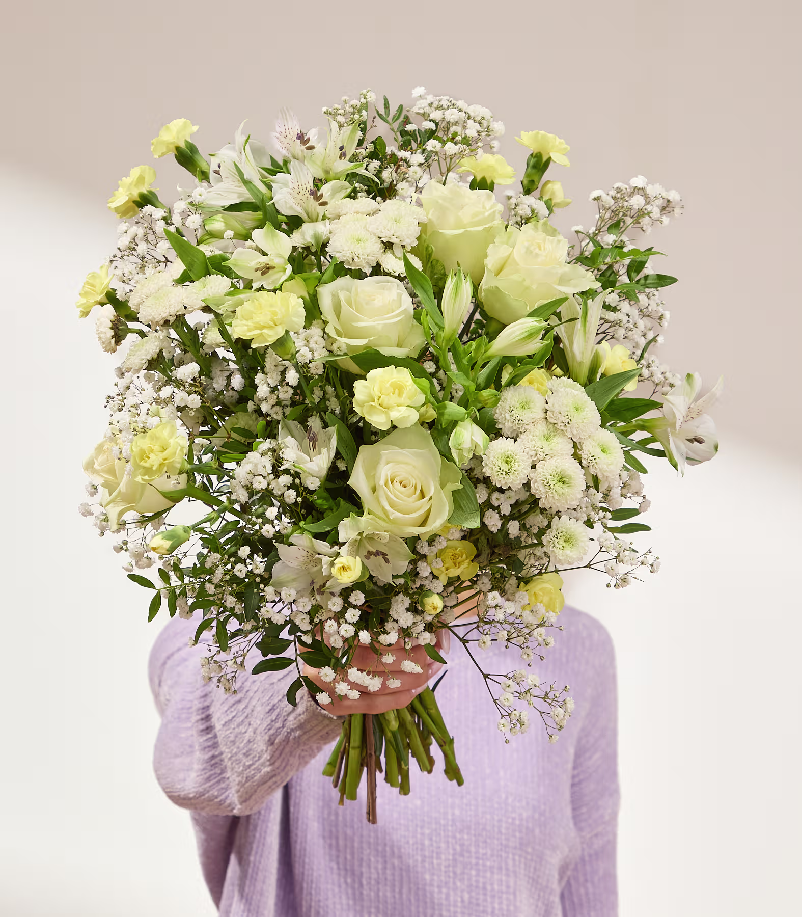 Auf einem Holztisch in einem gemütlichen Wohnzimmer steht eine Vase, gefüllt mit einem farbenprächtigen Strauß rosa Rosen und anderer Blumen; im Hintergrund sind ein Sofa und ein Fenster zu sehen. (Beschreibungstext KI-generiert)