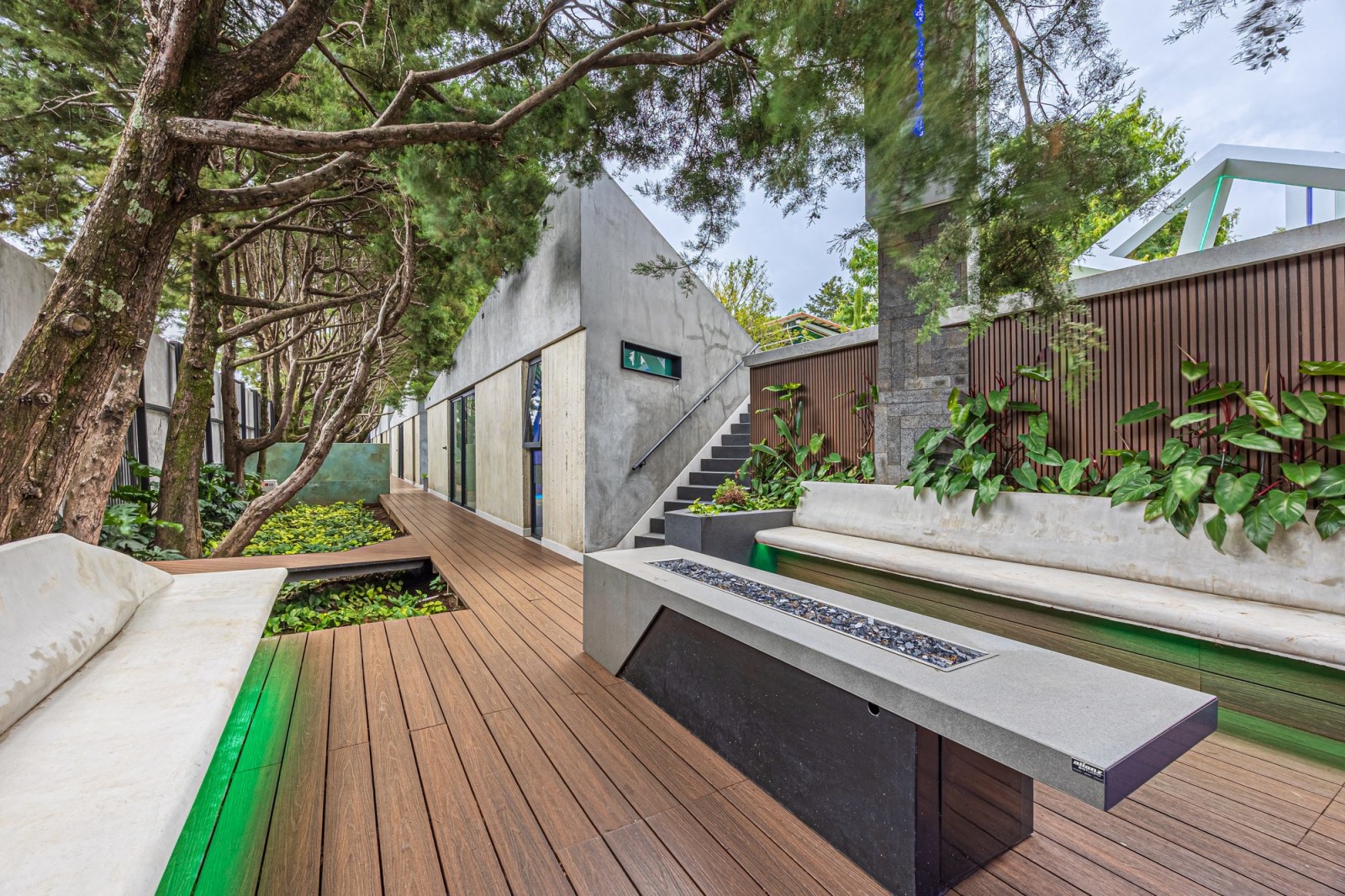 Wooden deck with built-in fire pit and concrete benches among trees.