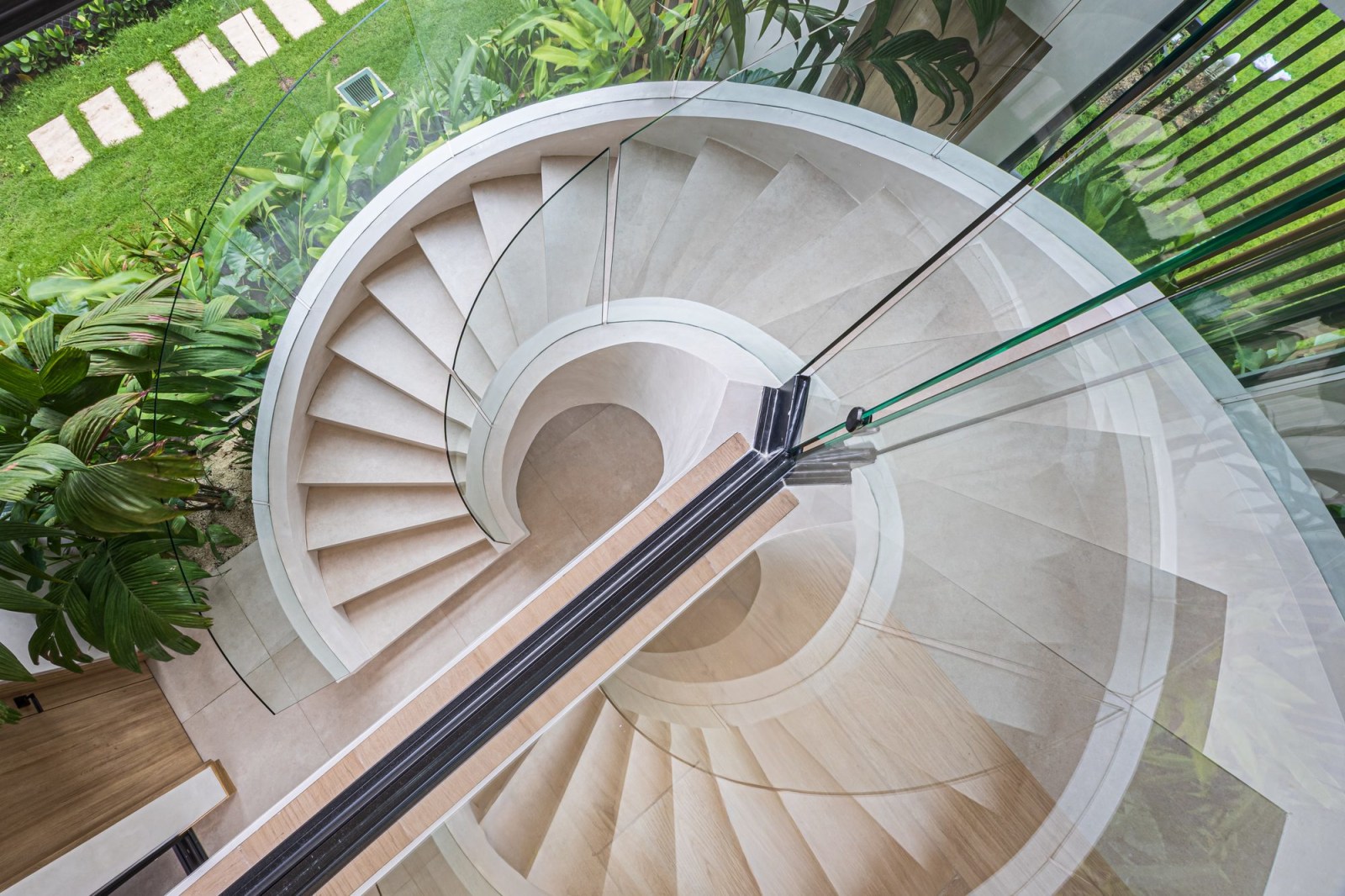 Aerial view of a spiral staircase with glass railing next to a tropical garden.