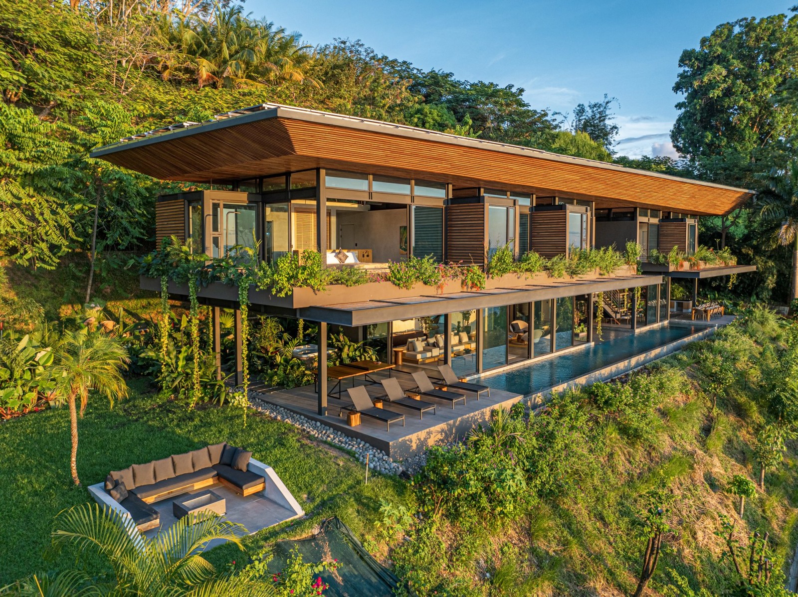 Modern two-story villa with infinity pool surrounded by tropical jungle at sunset.