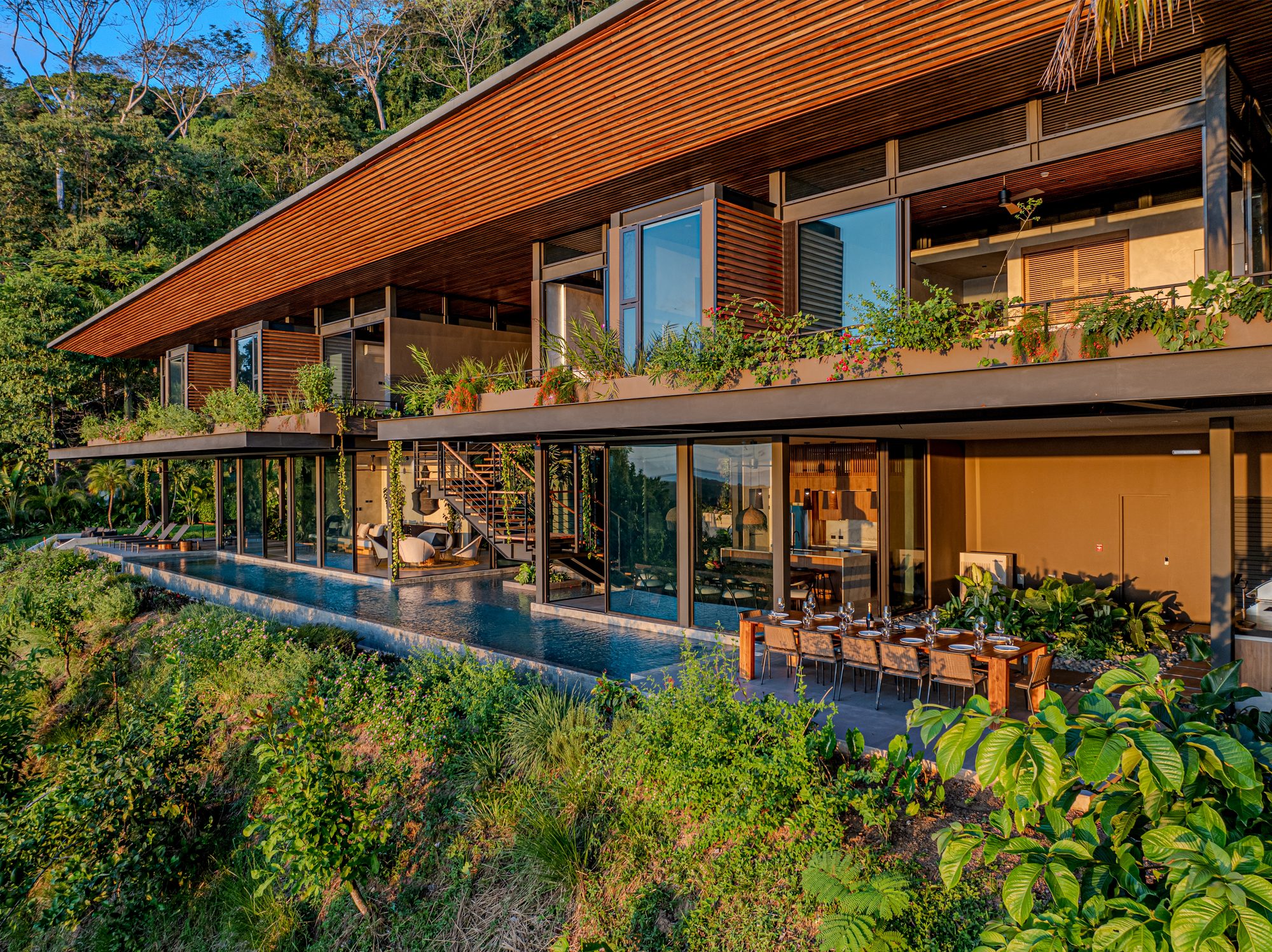 Modern villa facade with infinity pool surrounded by tropical jungle at sunset.